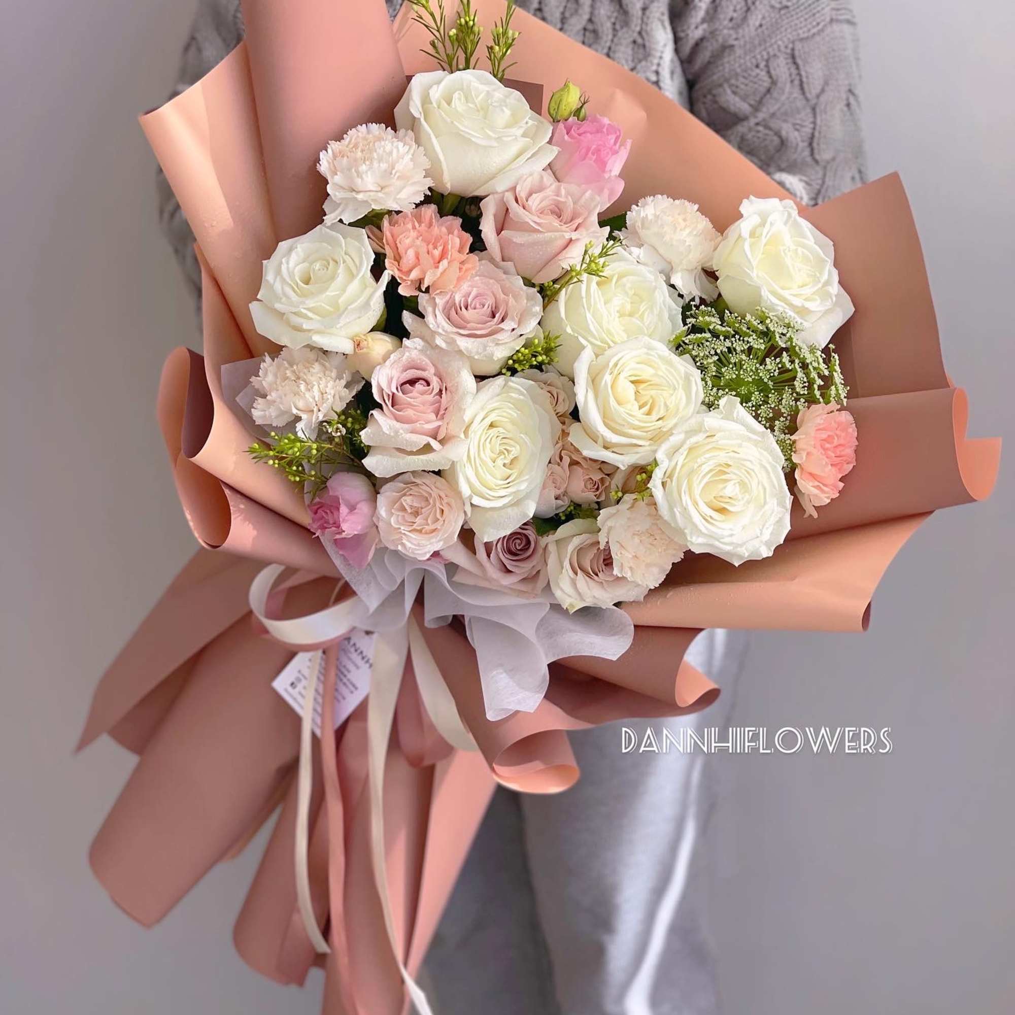 Bouquet of white and blush roses with carnations wrapped in peach paper