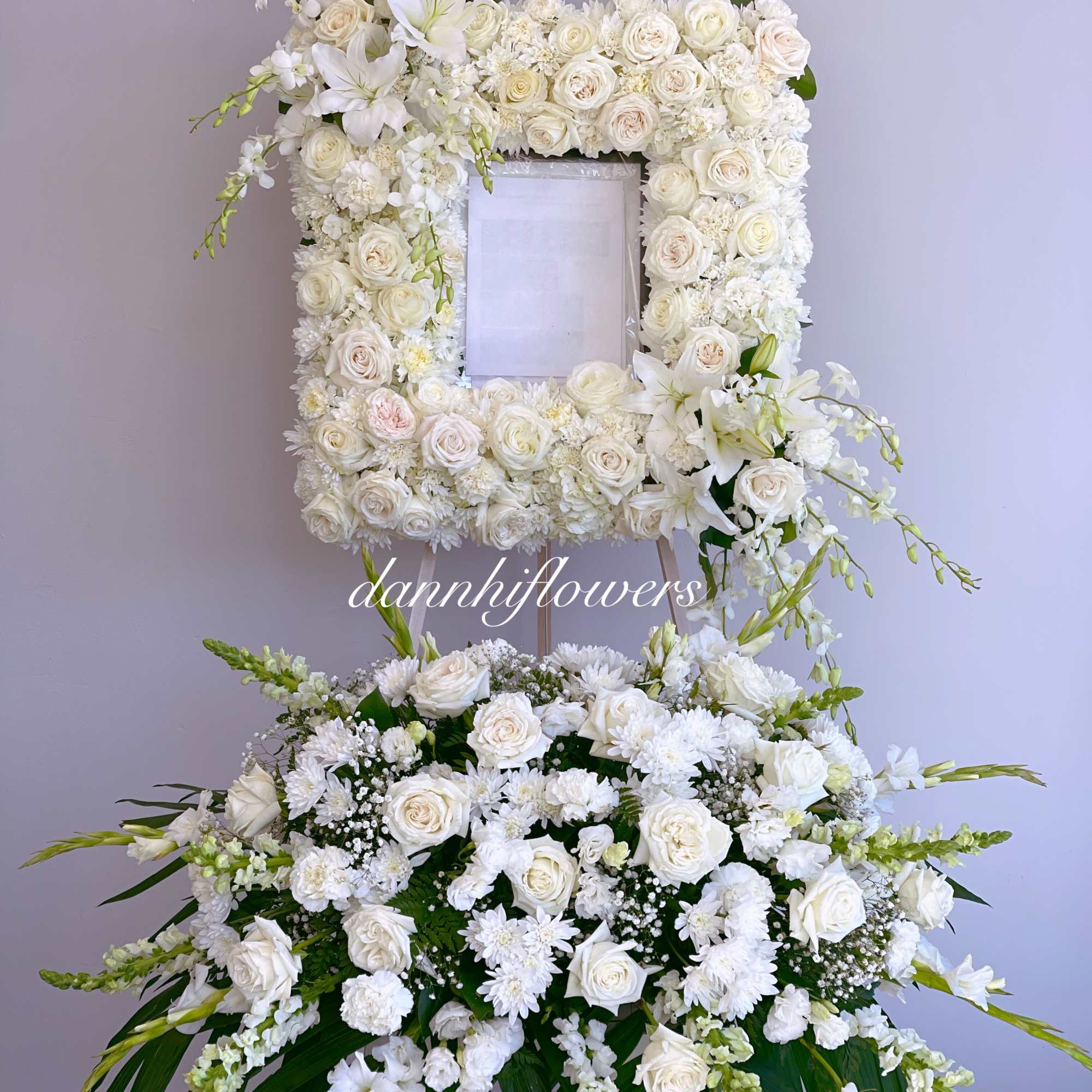 White floral standing arrangement with roses and lilies around a framed center