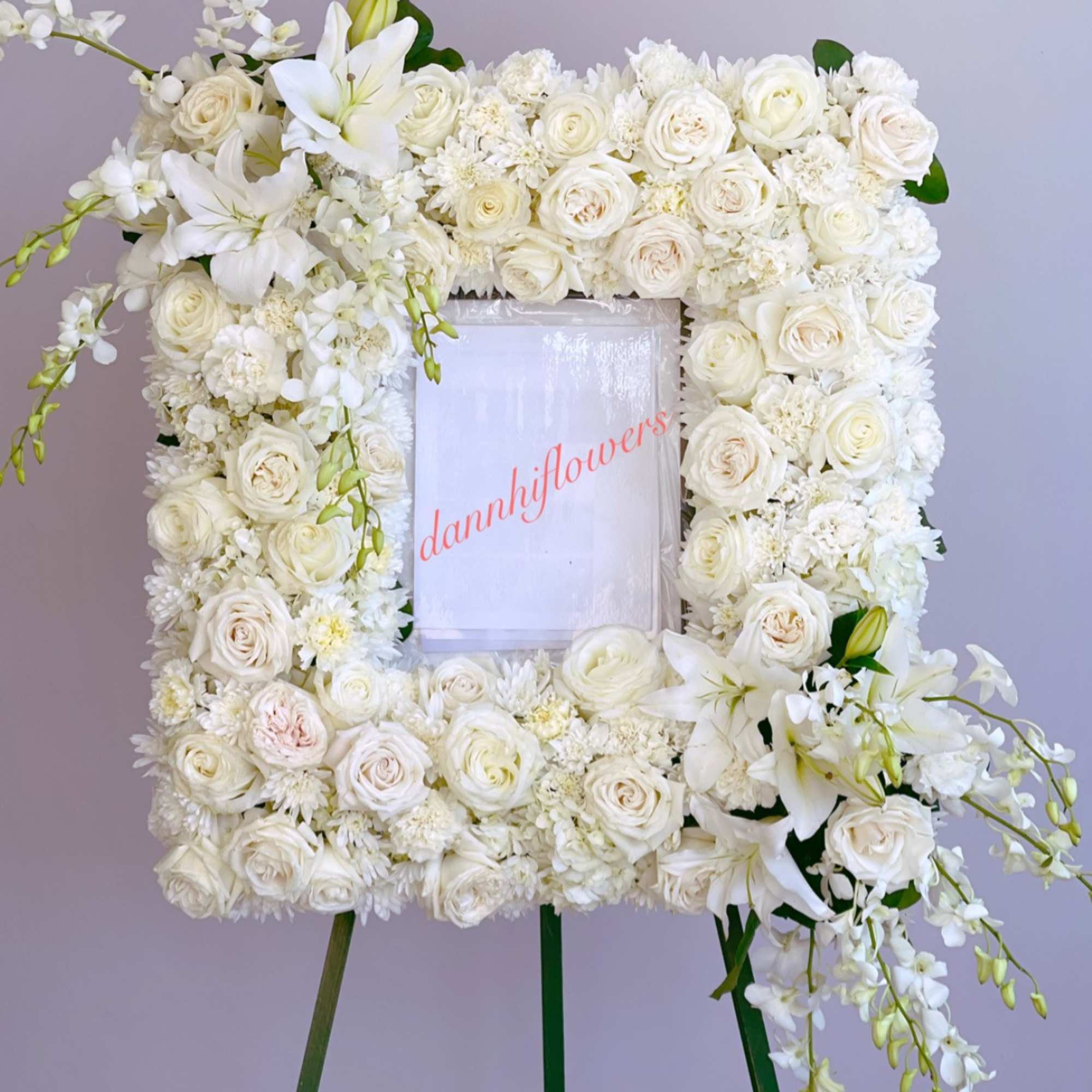 White floral wreath on an easel with roses and lilies