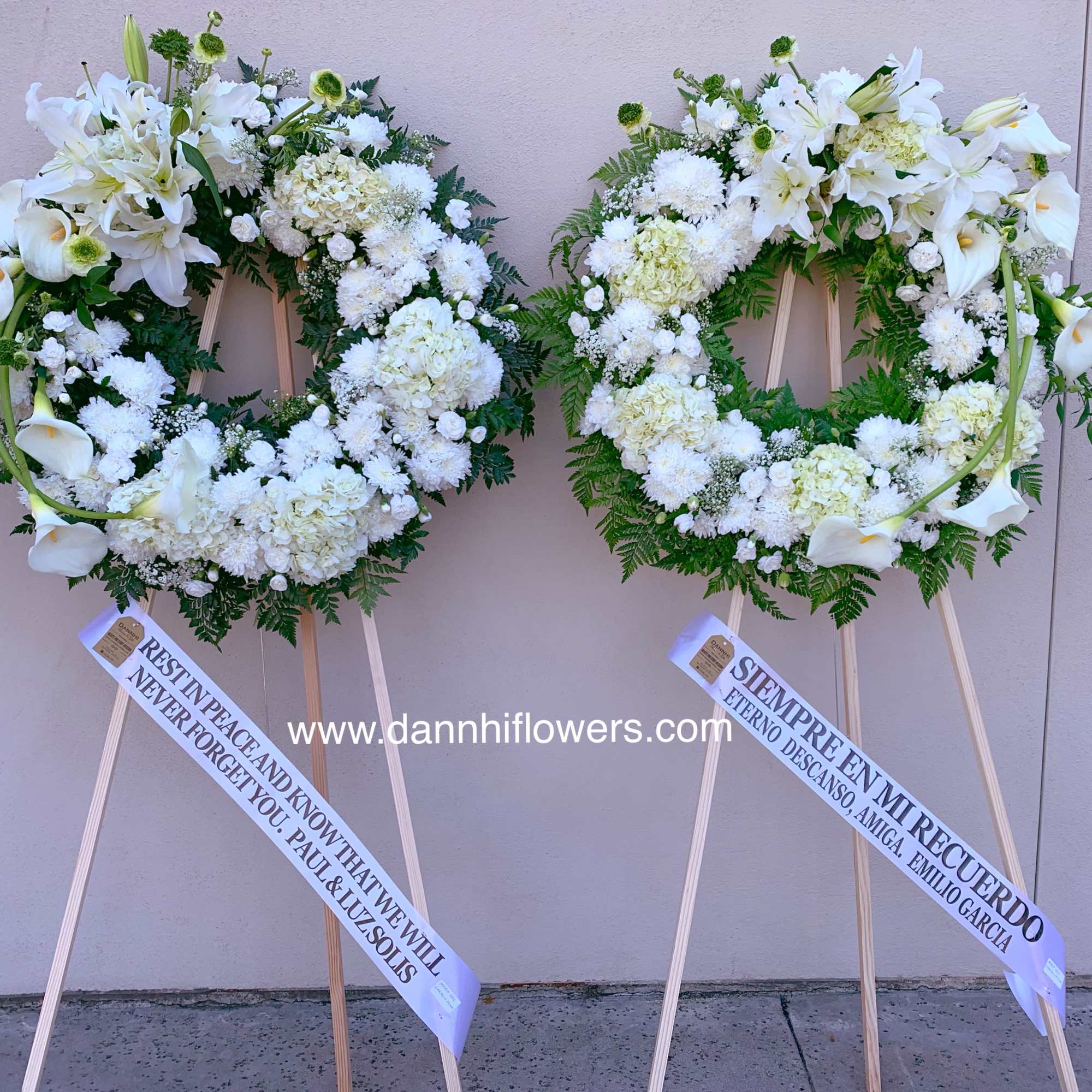 Two white funeral wreaths on wooden stands with ribbon banners.