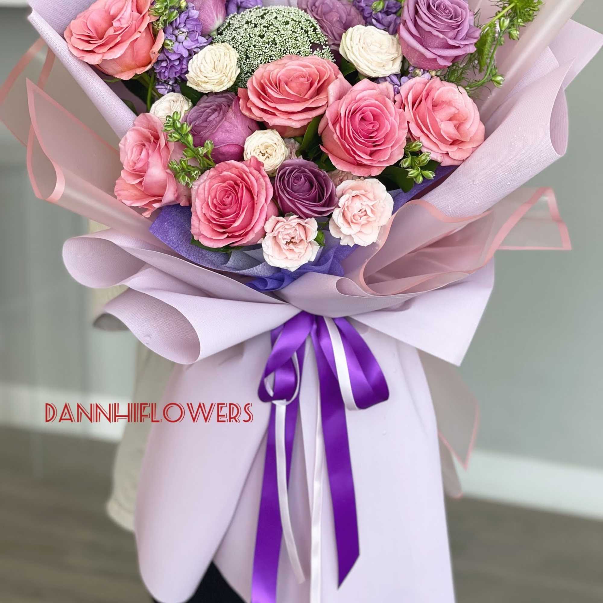 Hand-tied bouquet of pink and purple roses wrapped in lavender paper