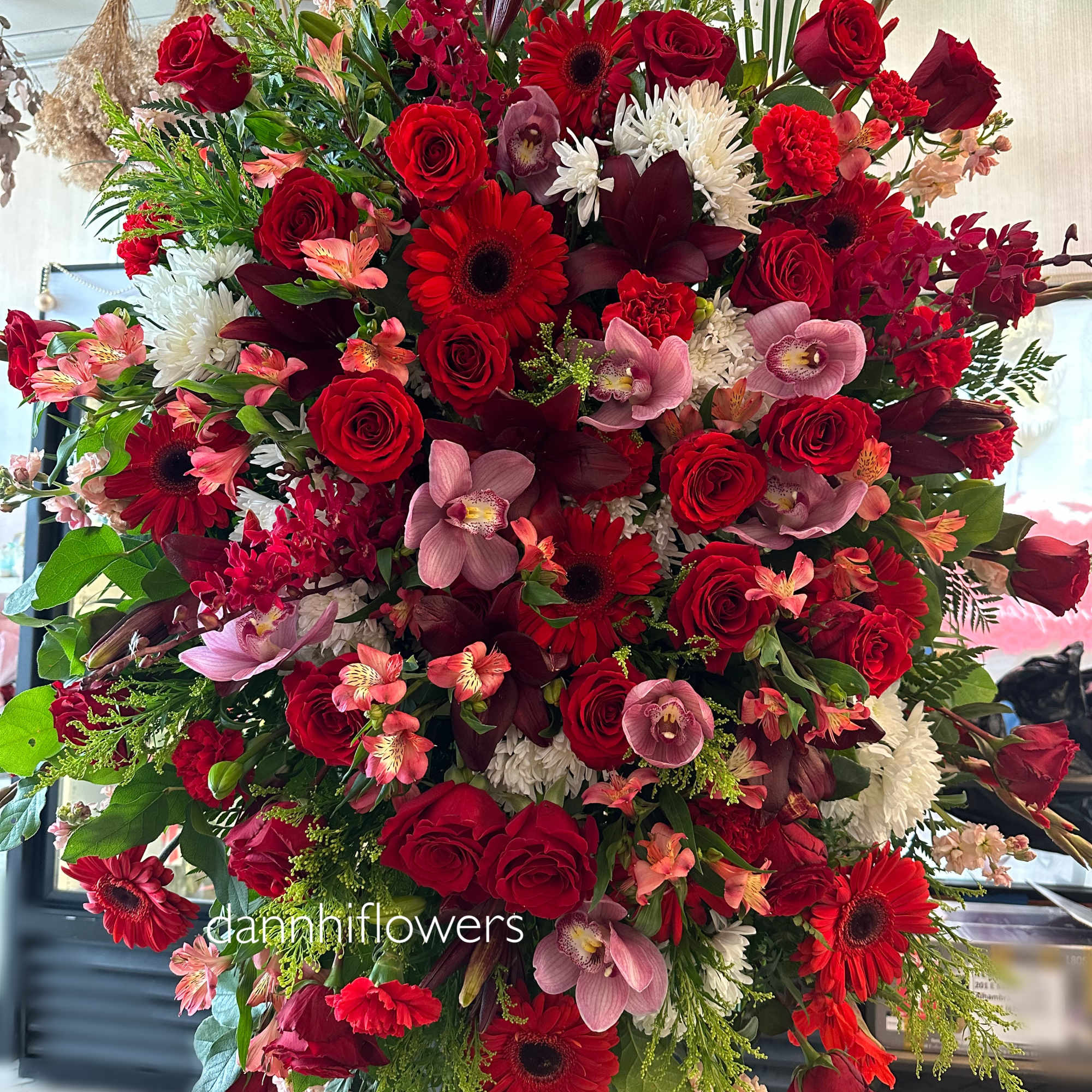 Large red floral standing spray with roses, gerberas, orchids, and white mums