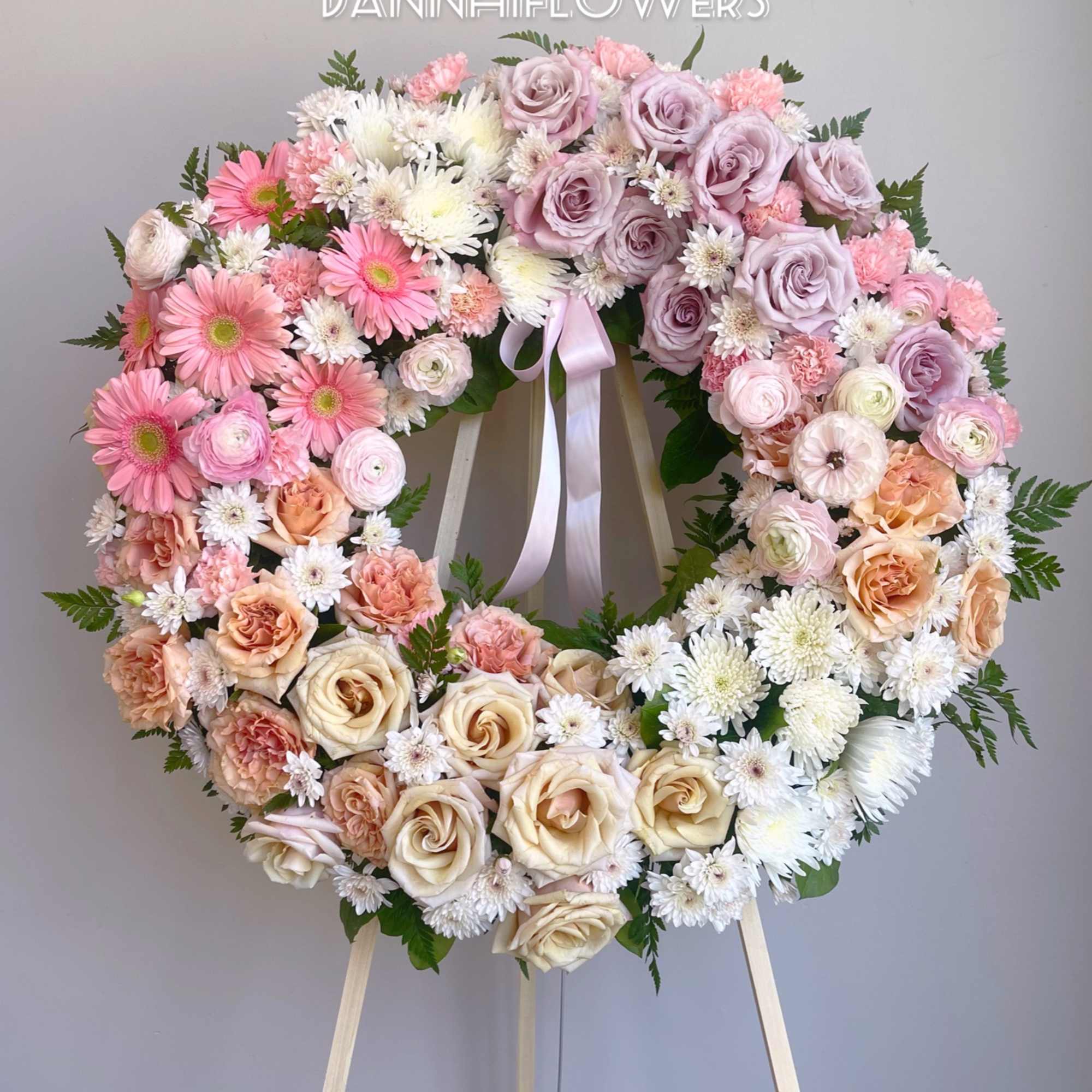 Heart-shaped floral wreath with pink, lavender, peach, and white blooms on an easel