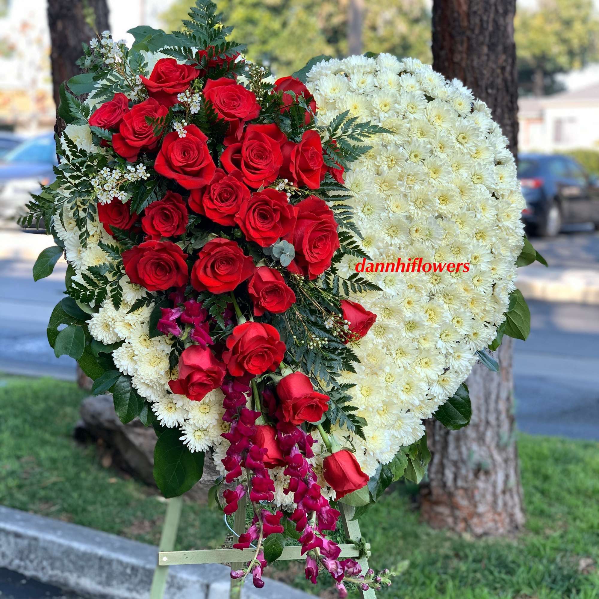 Heart-shaped floral tribute with red roses and white chrysanthemums on an easel
