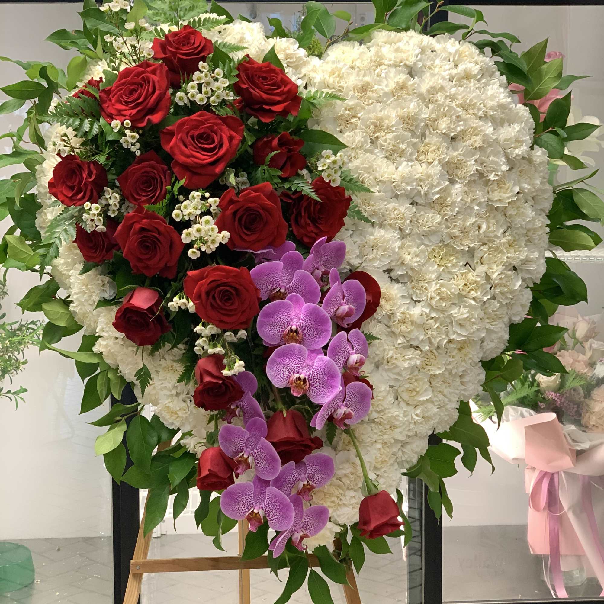 Heart-shaped floral wreath with red roses, white blooms, and purple orchids on an easel