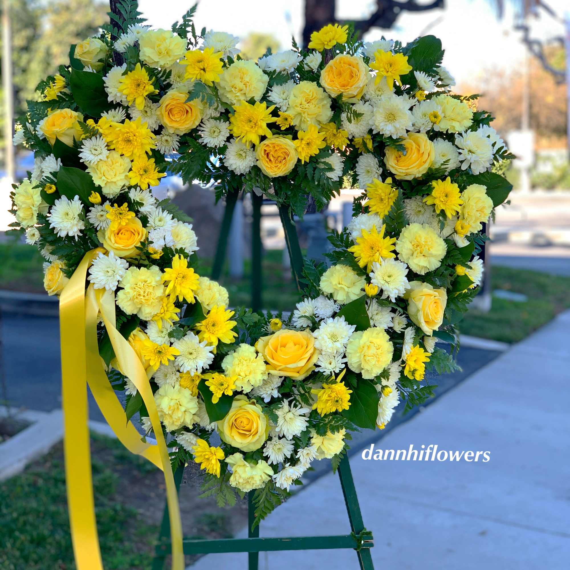 Heart-shaped floral wreath with yellow and white flowers on an easel