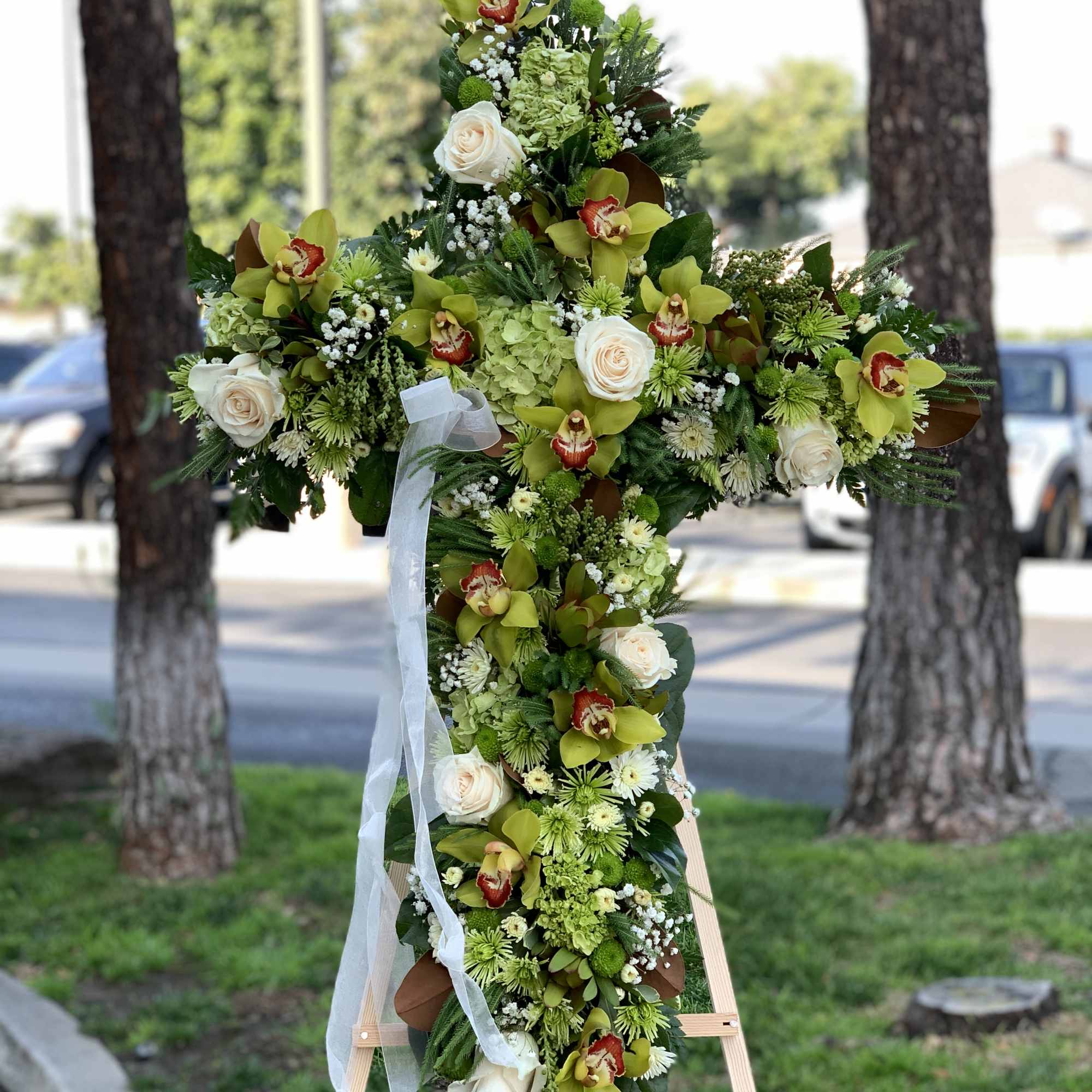 Large floral cross on an easel with white roses and green orchids