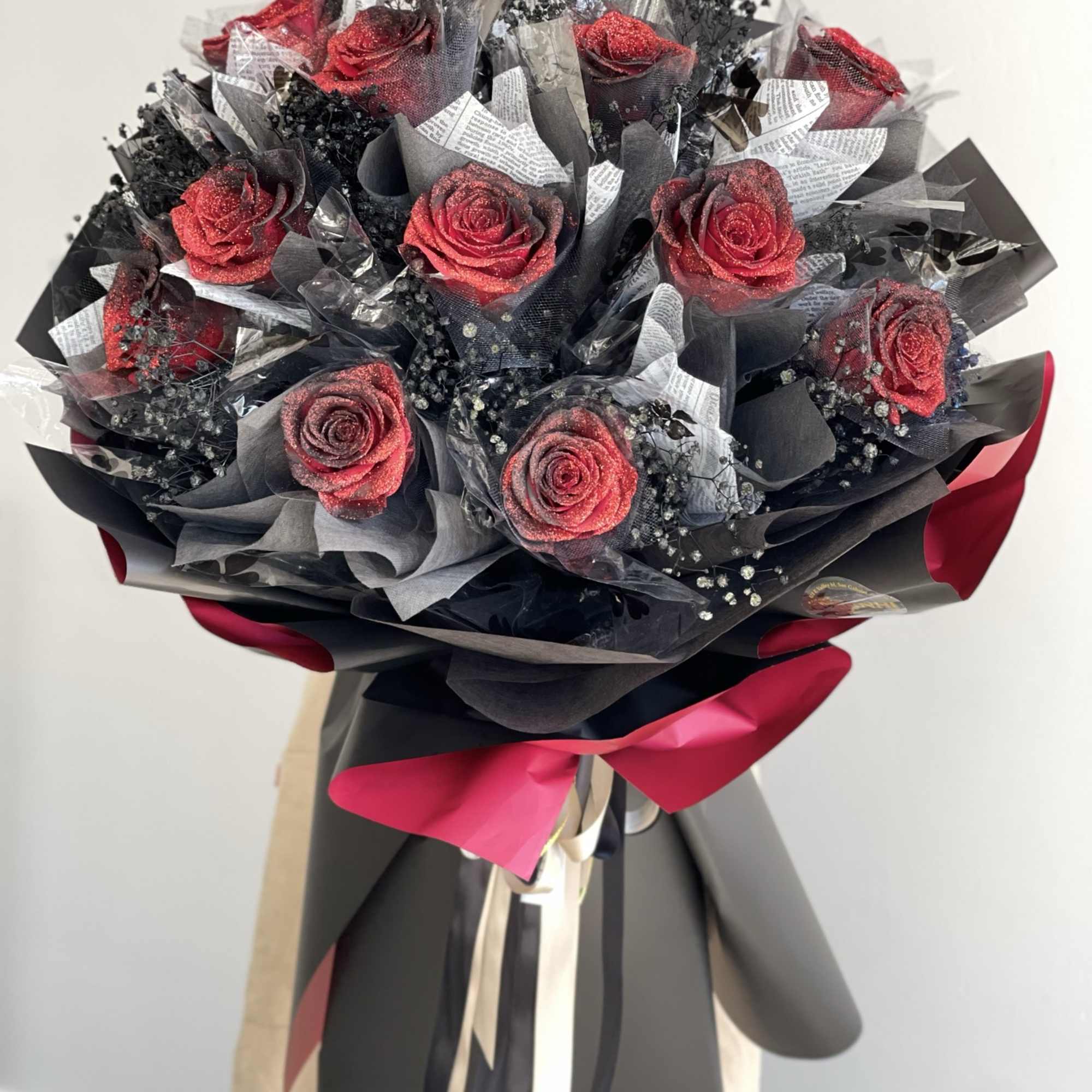 Bouquet of red roses wrapped in black paper with a pink ribbon
