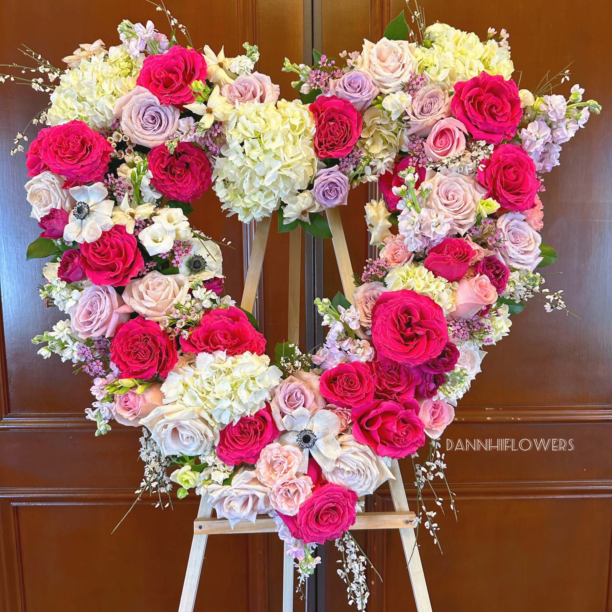 Heart-shaped floral arrangement of pink, lavender, and white roses on an easel
