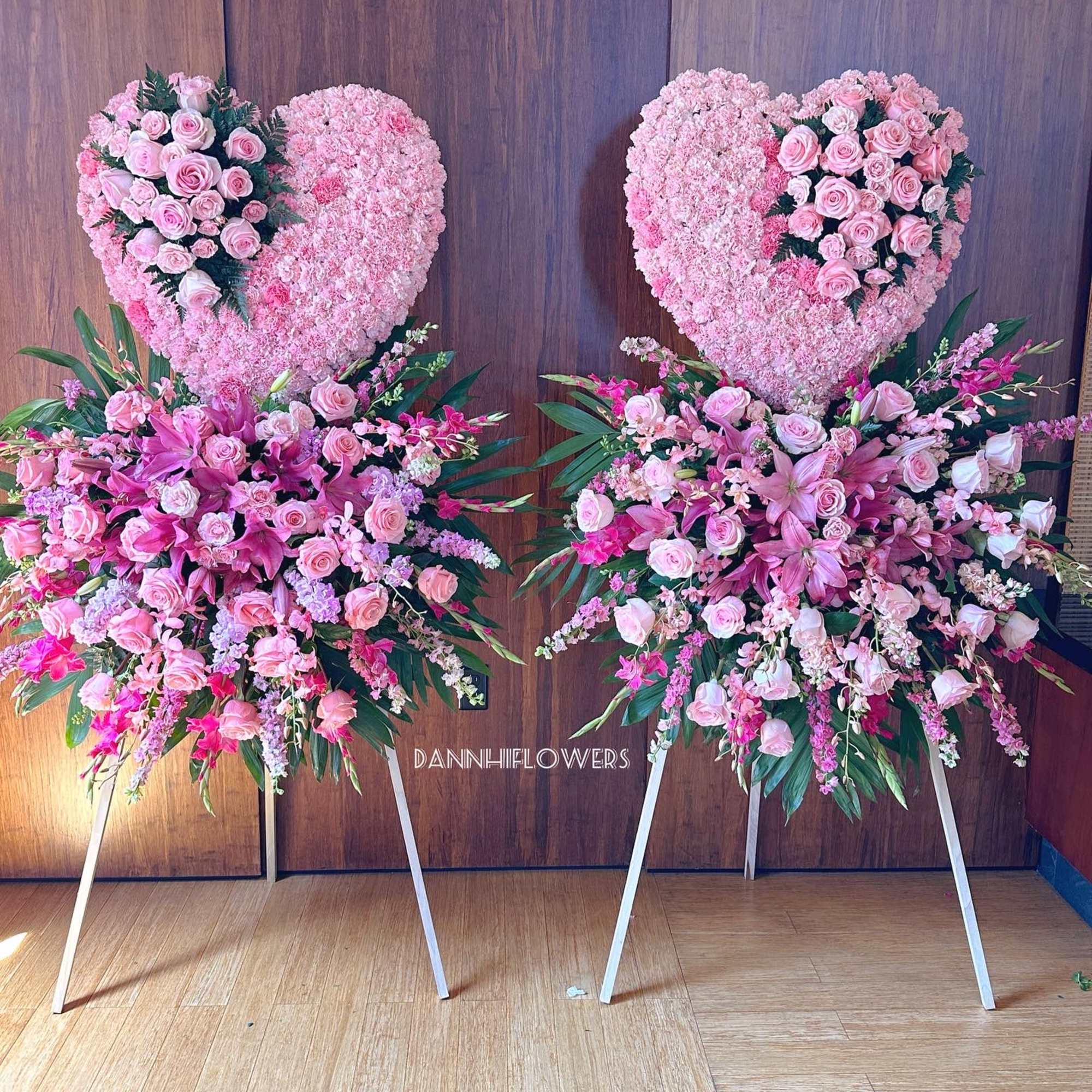 Two pink heart-shaped floral stands with matching bouquets on easels