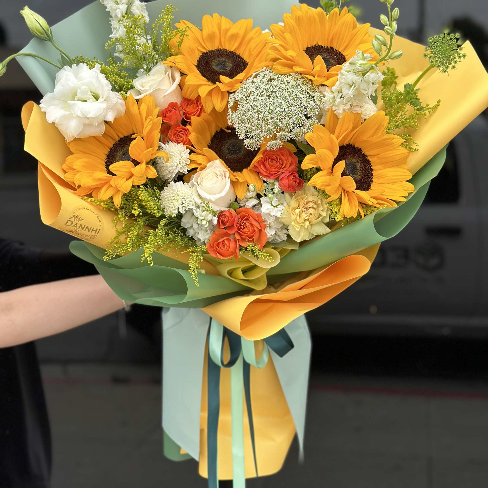 Bouquet of sunflowers, roses, and white blooms wrapped in yellow and green paper