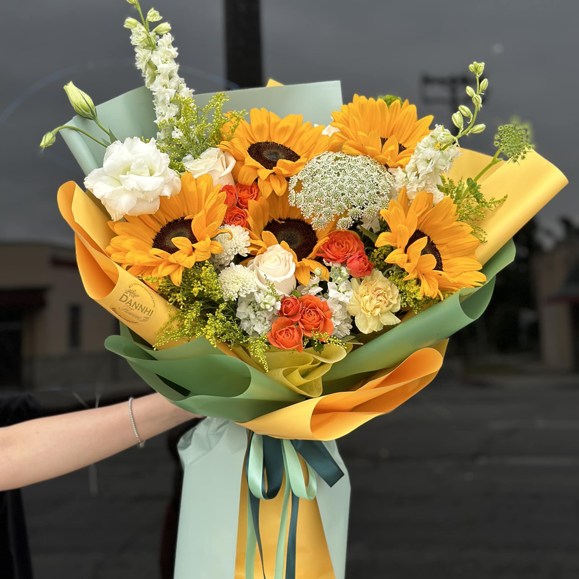 Bouquet of sunflowers, white roses, and orange spray roses wrapped in pastel paper