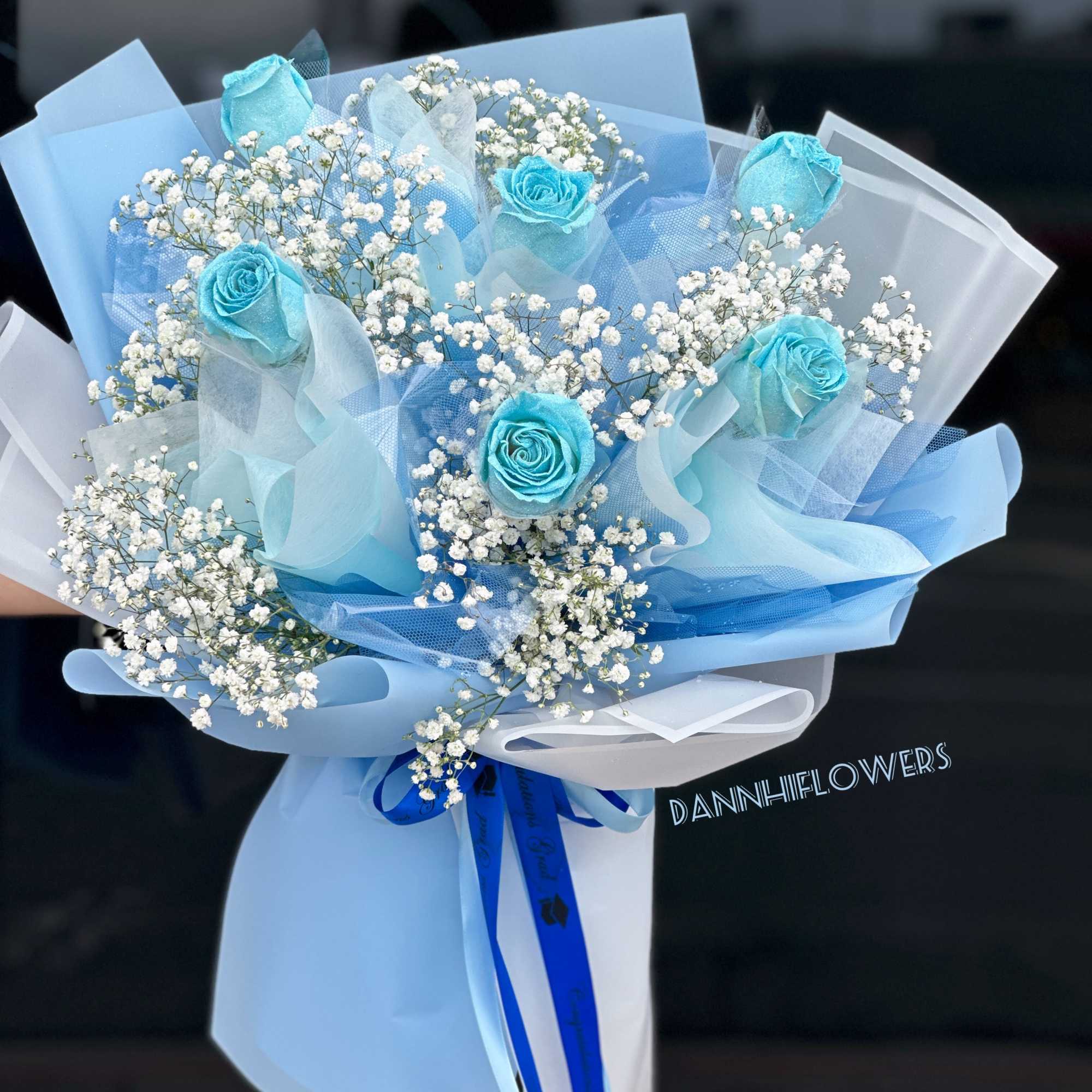 Bouquet of blue roses and white baby's breath wrapped in pale blue paper