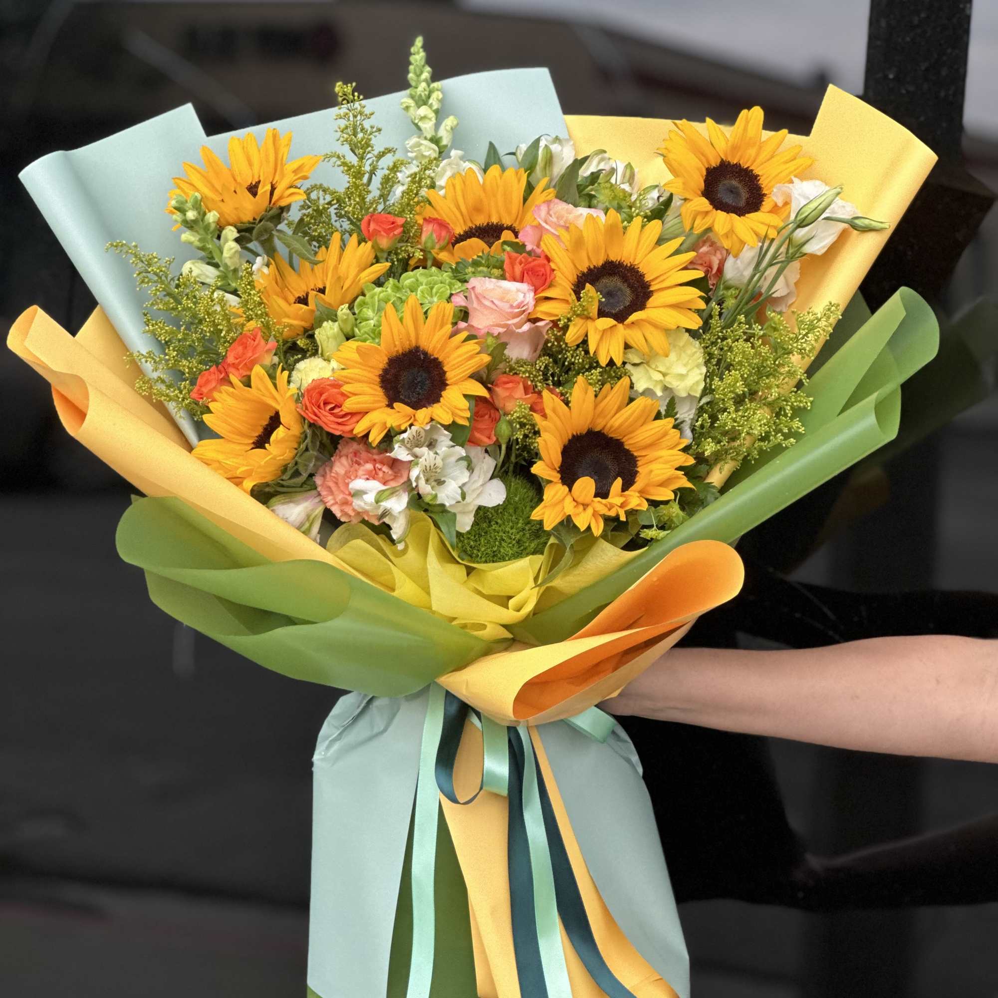Bouquet of sunflowers and mixed pastel flowers wrapped in colorful paper