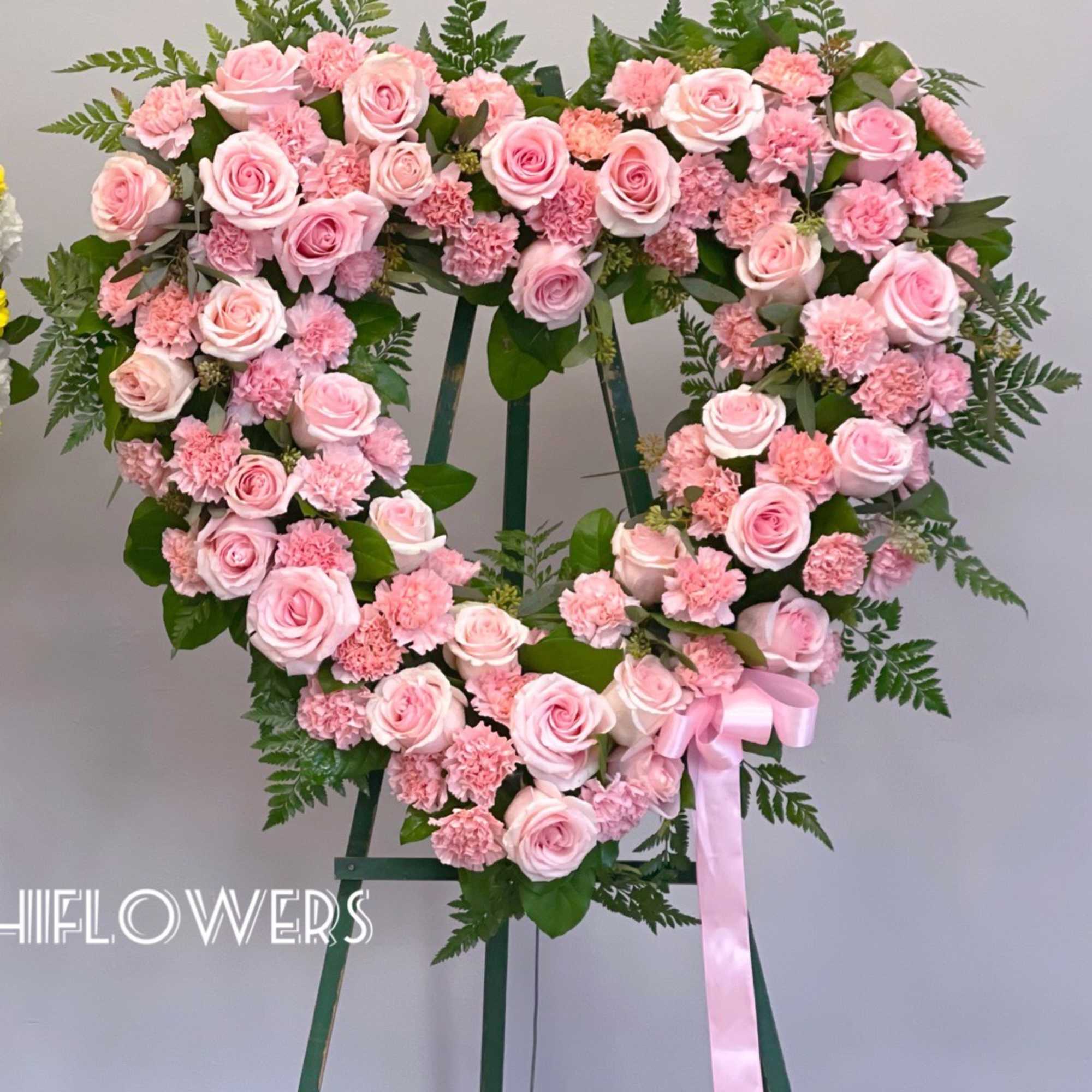 Heart-shaped pink rose and carnation wreath on a stand with a ribbon