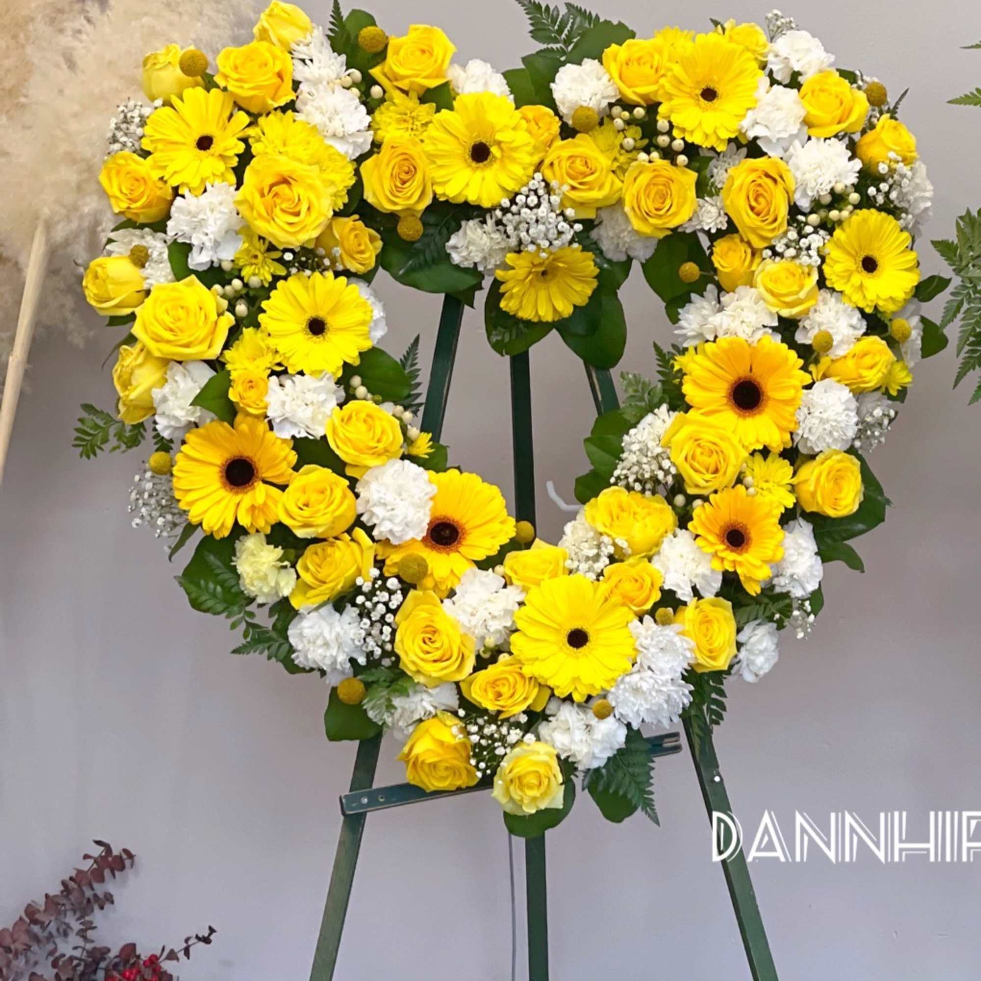 Heart-shaped yellow floral wreath on a stand with roses and daisies