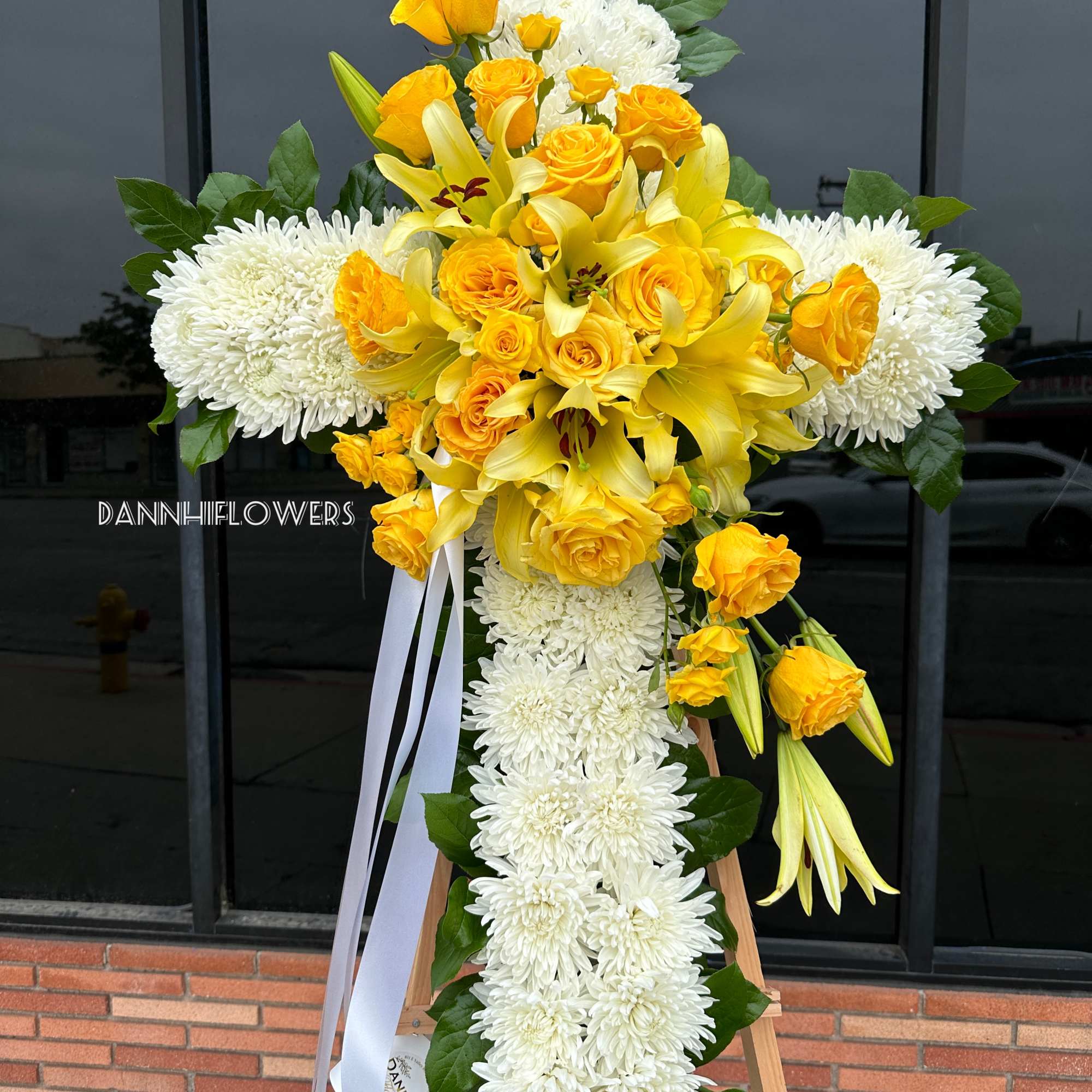 Yellow roses and lilies with white chrysanthemums on a standing cross arrangement