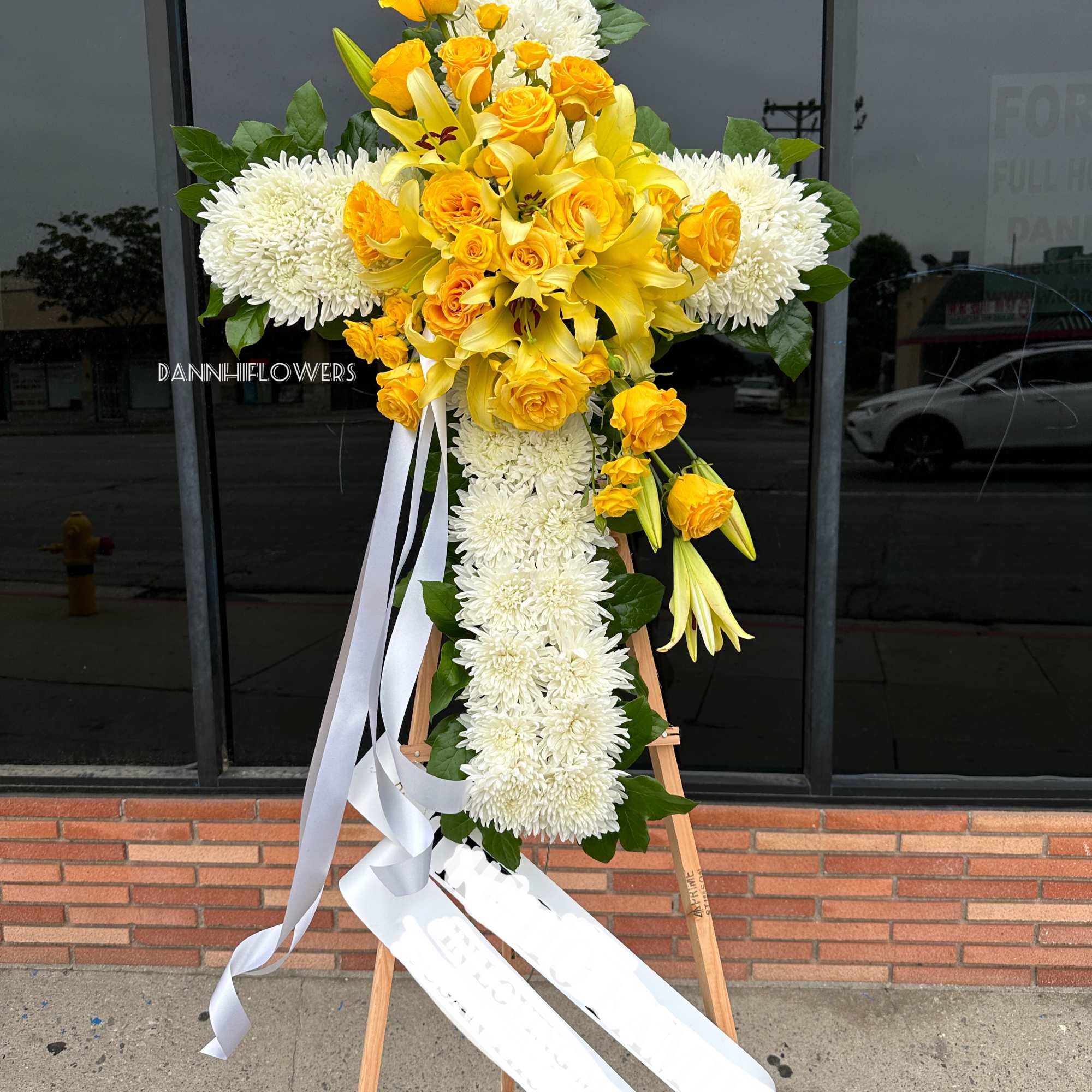 Yellow roses and lilies arranged in a white floral cross on an easel