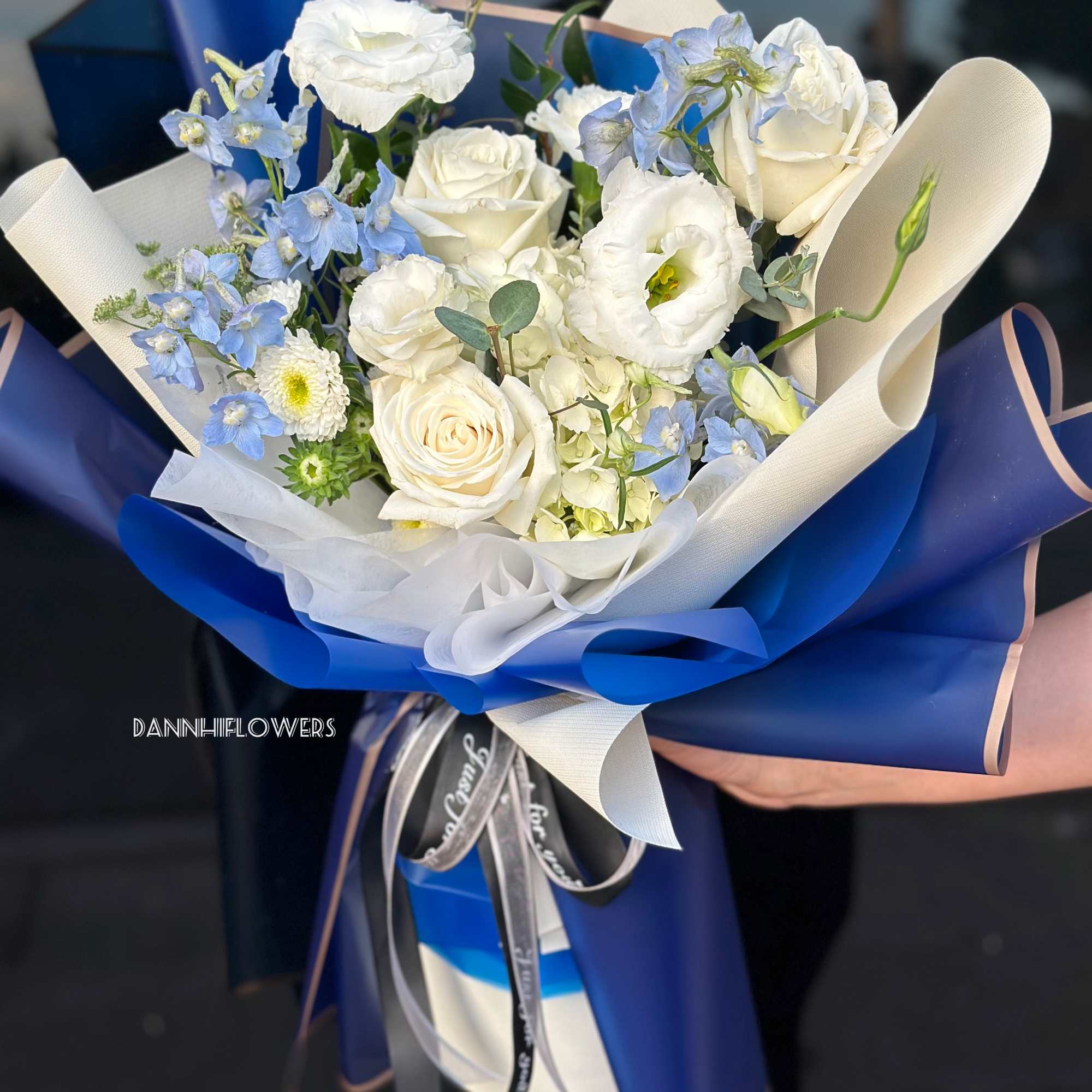 Bouquet of white roses and pale blue flowers wrapped in blue paper