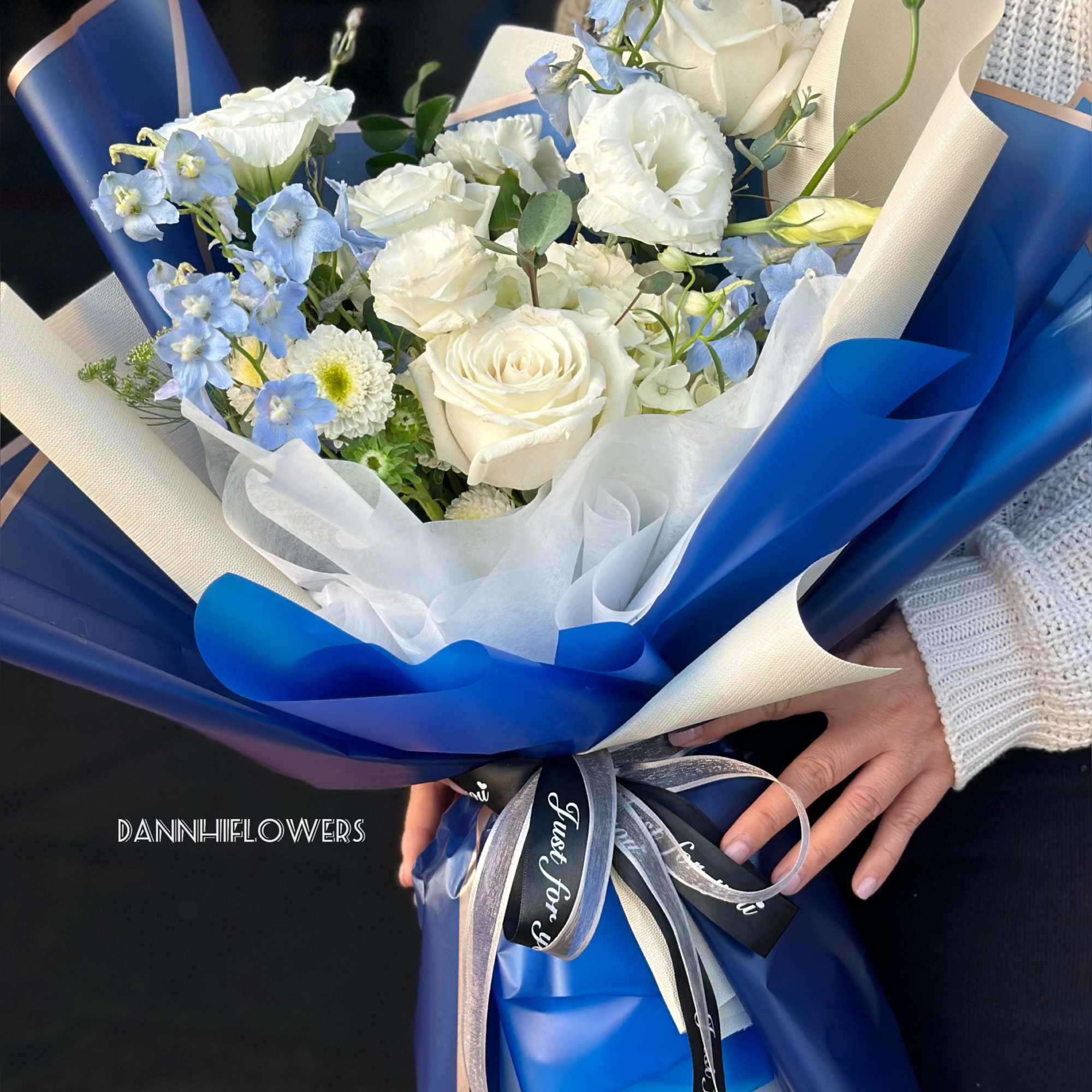 Bouquet of white roses and light blue flowers wrapped in blue and cream paper