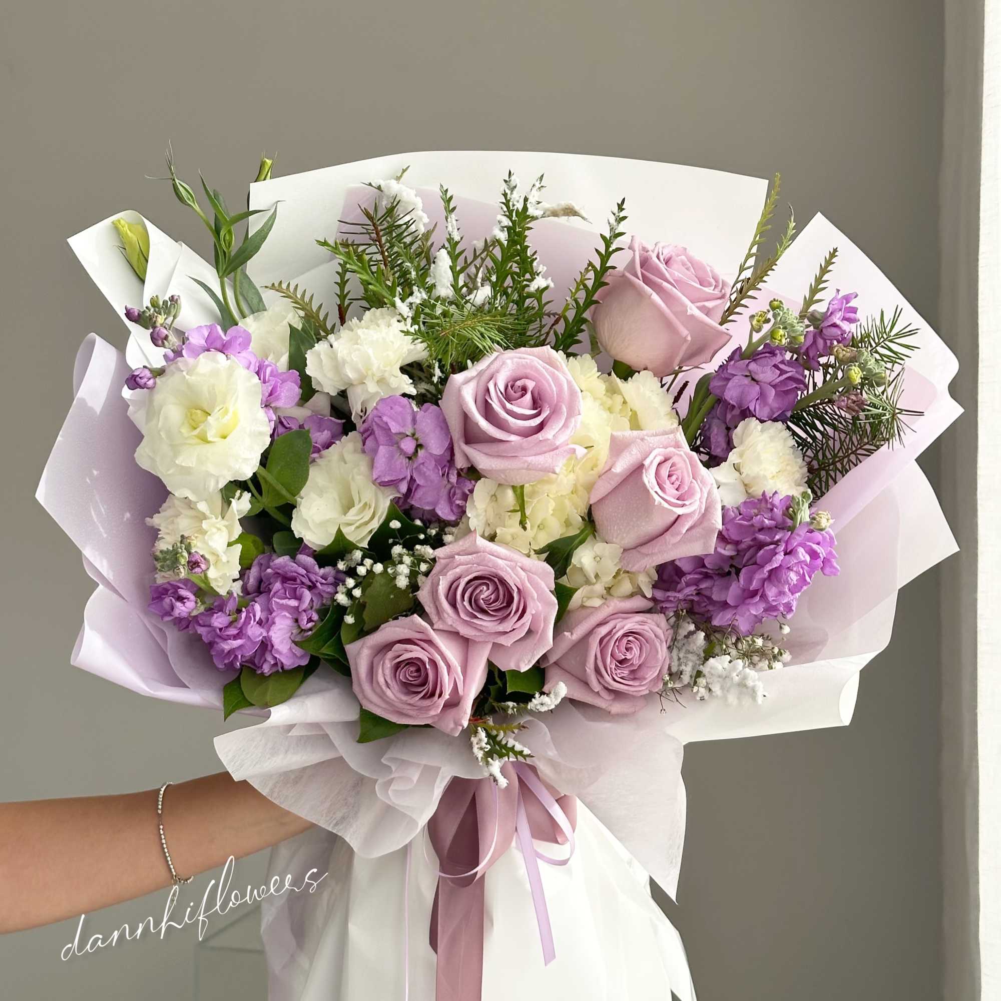 Hand-tied bouquet of lavender roses and purple-white blooms wrapped in pastel paper