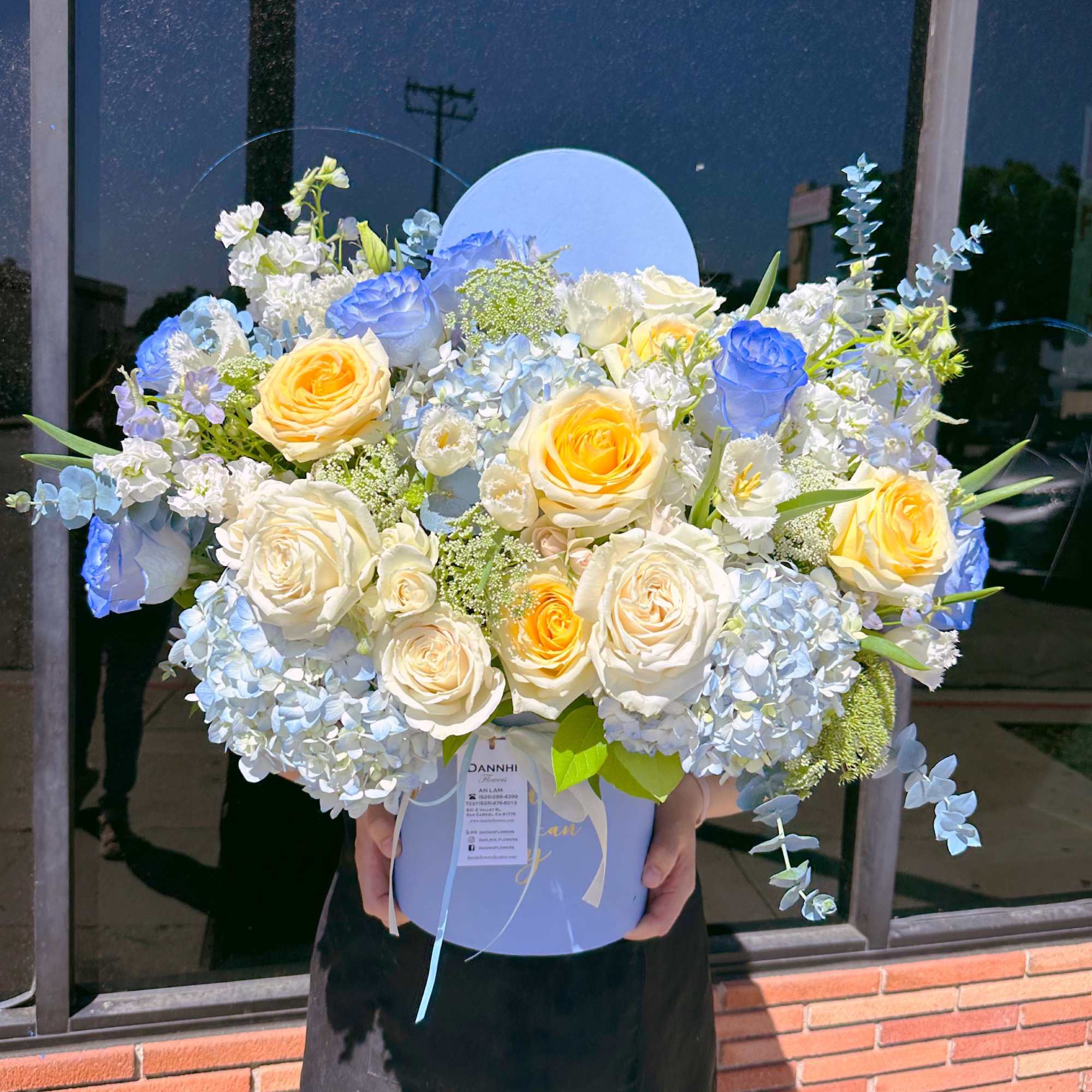 Large bouquet of blue, white, and yellow roses in a round box