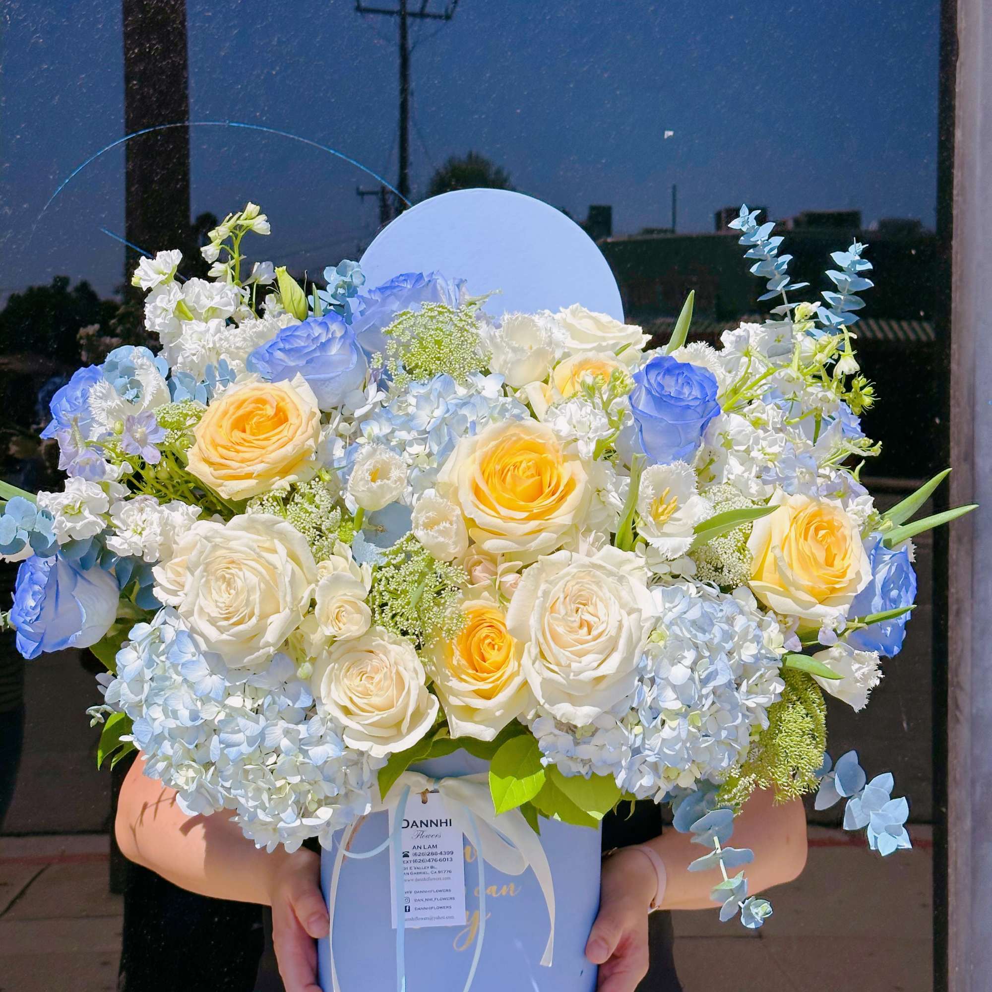 Large pastel bouquet of blue, white, and yellow roses in a round box