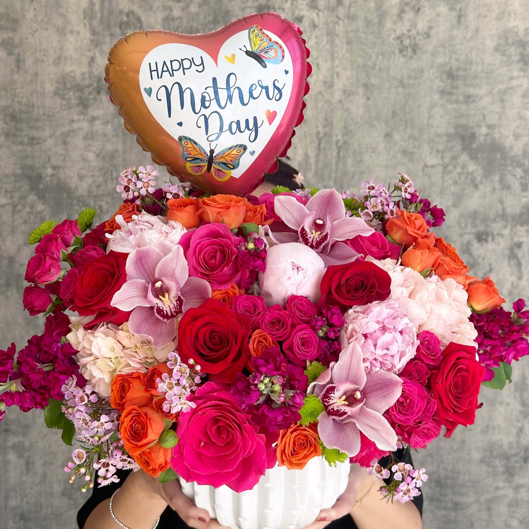Heart-shaped Mother's Day balloon above a colorful flower arrangement in a white vase