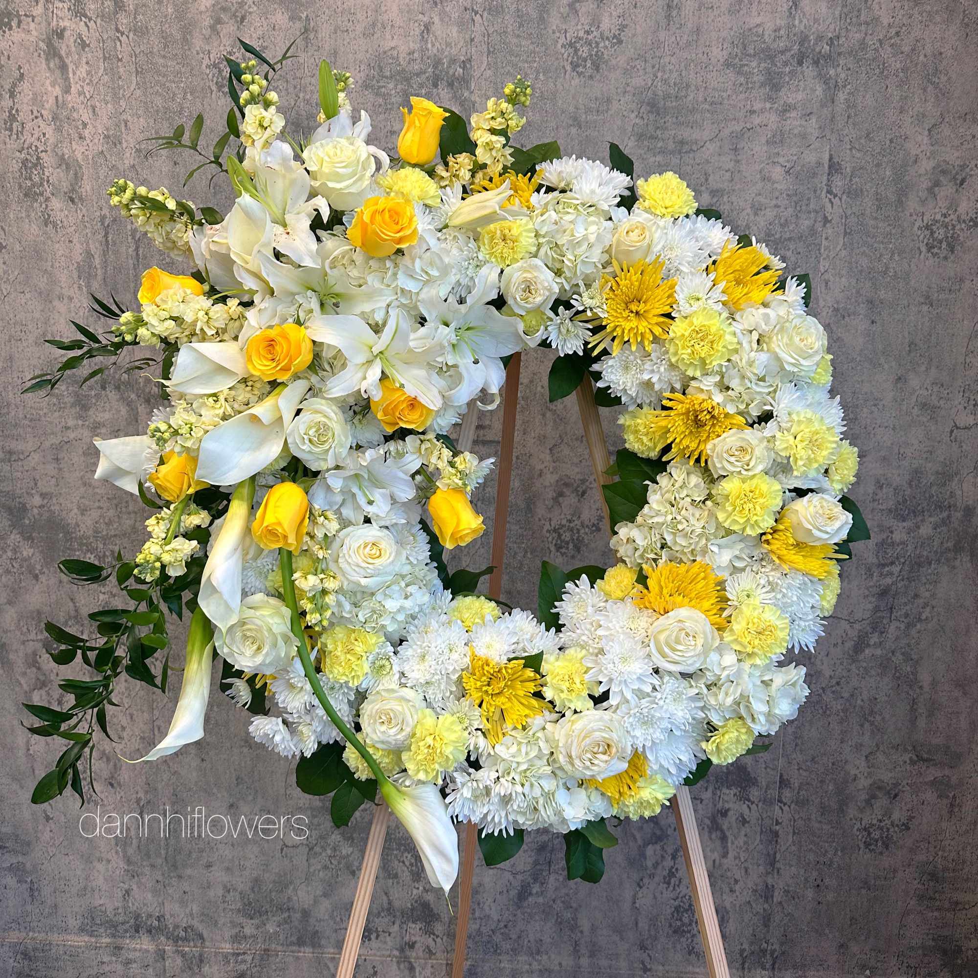 Large floral wreath on a wooden easel with white and yellow flowers