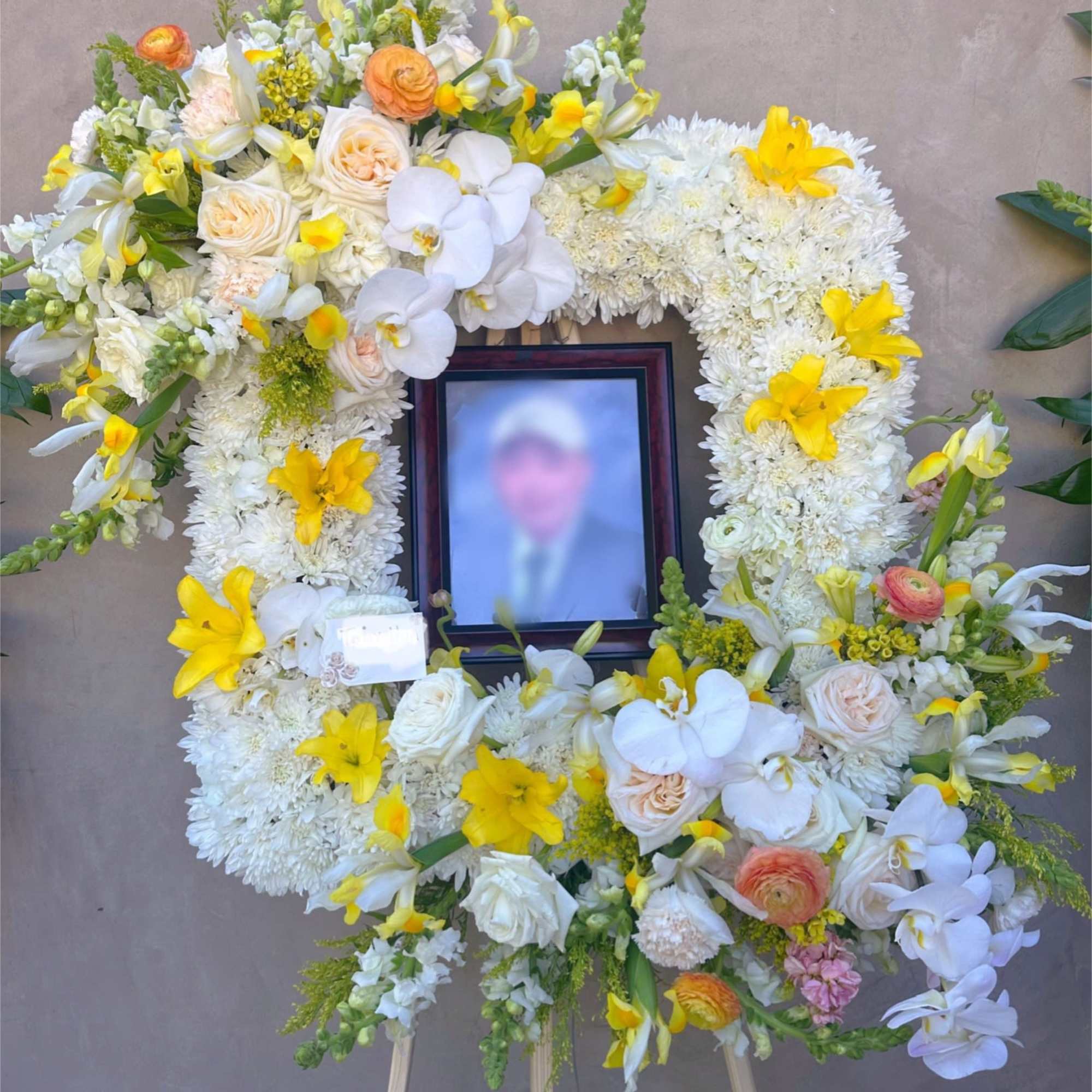 Large white and yellow floral funeral wreath on an easel with a framed photo in the center