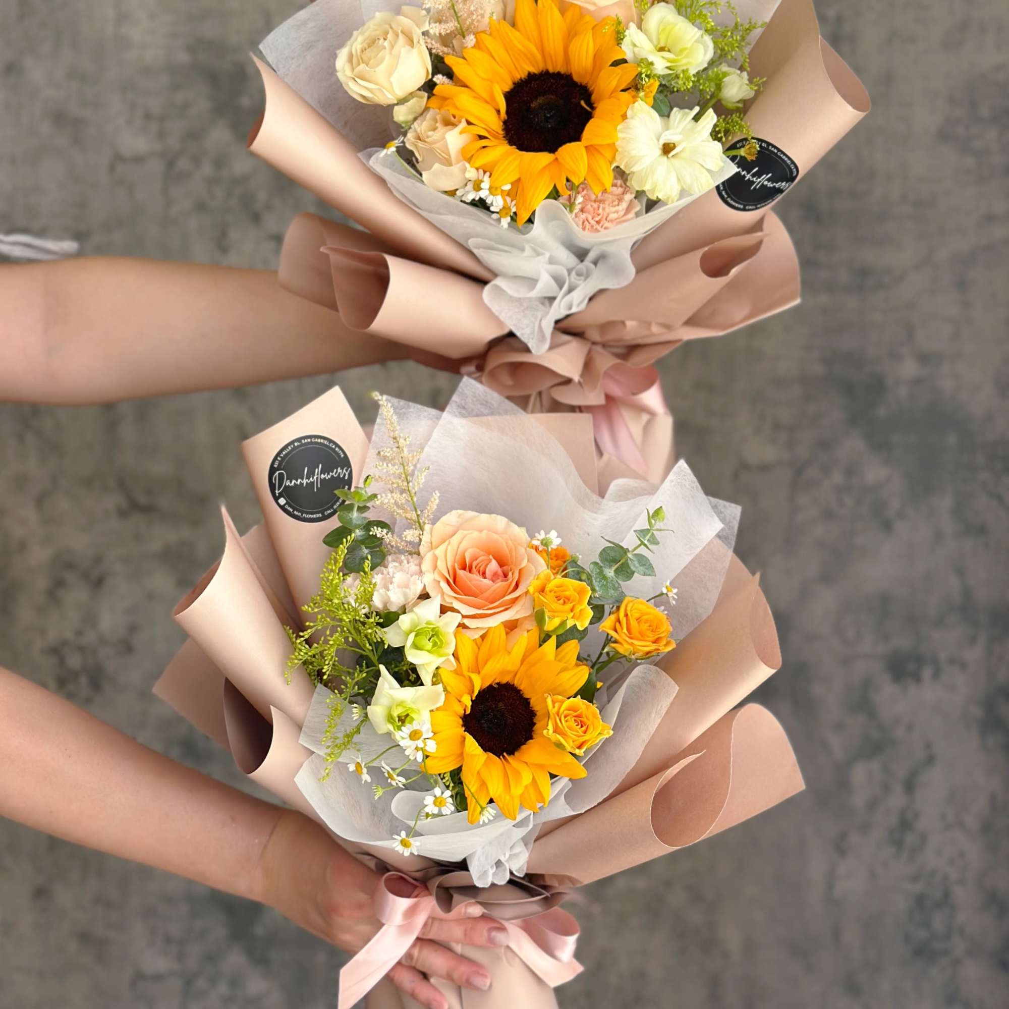 Two hand-tied bouquets with sunflowers and roses wrapped in blush paper