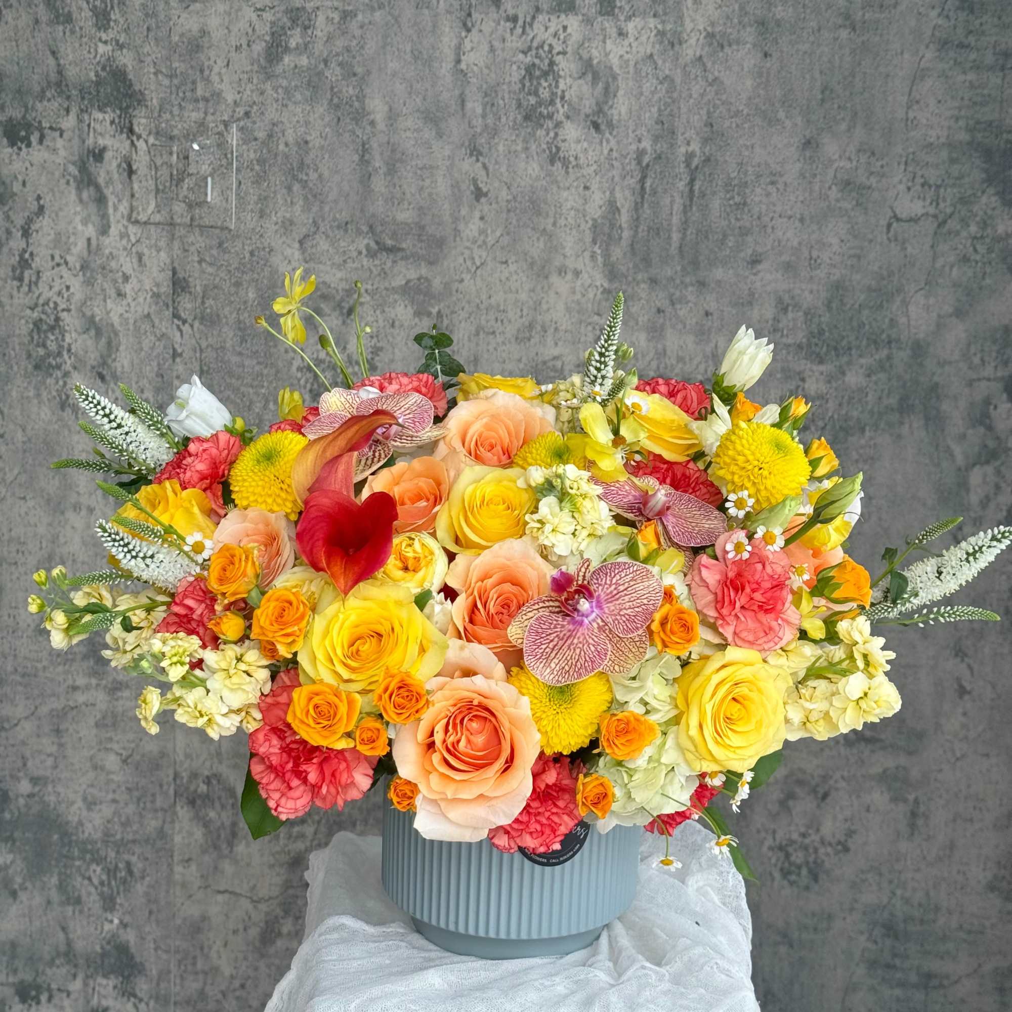 Large mixed bouquet in a ribbed blue vase with yellow, peach, pink, and white blooms