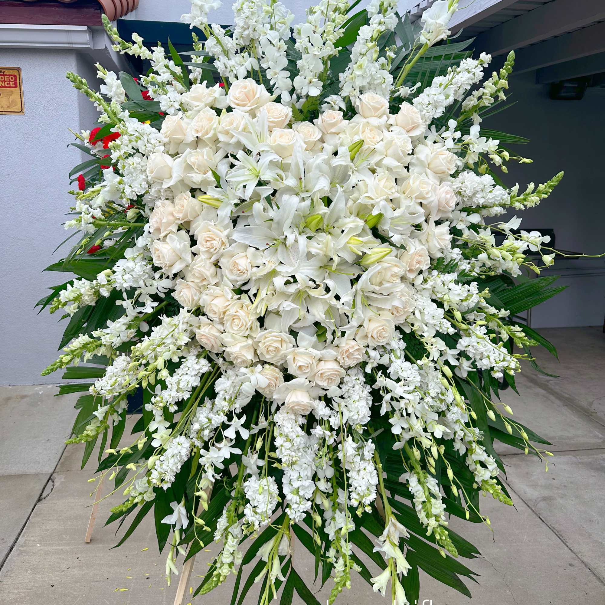 Large white funeral spray with roses and lilies on a stand
