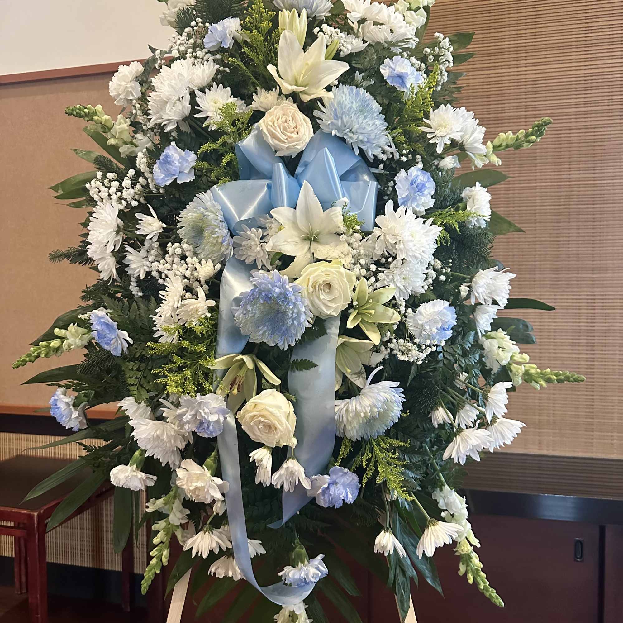 Large white and pale blue funeral spray on an easel