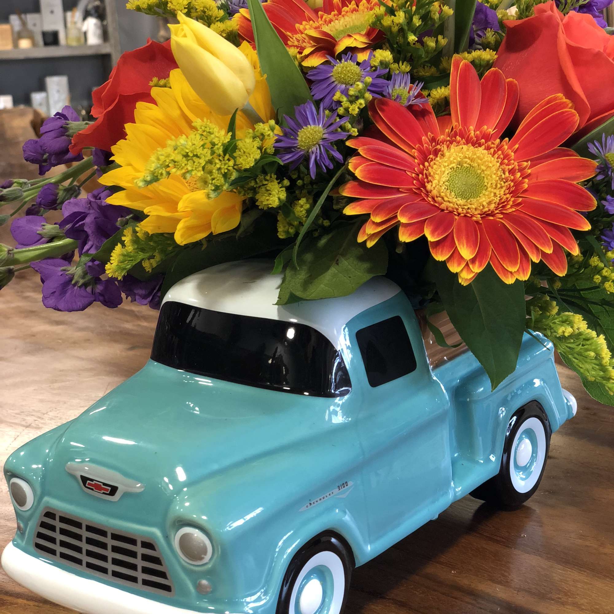 Colorful mixed flower arrangement in a turquoise truck-shaped vase