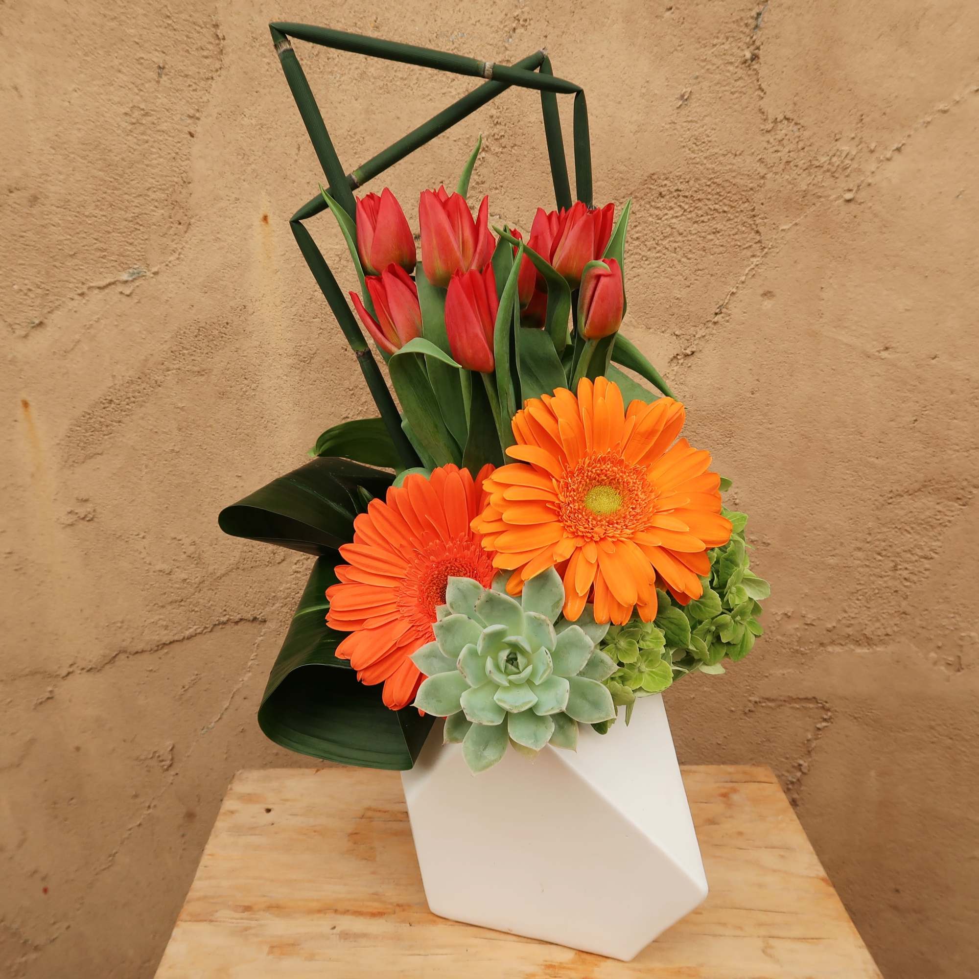 Orange gerbera daisies and red tulips in a white geometric vase