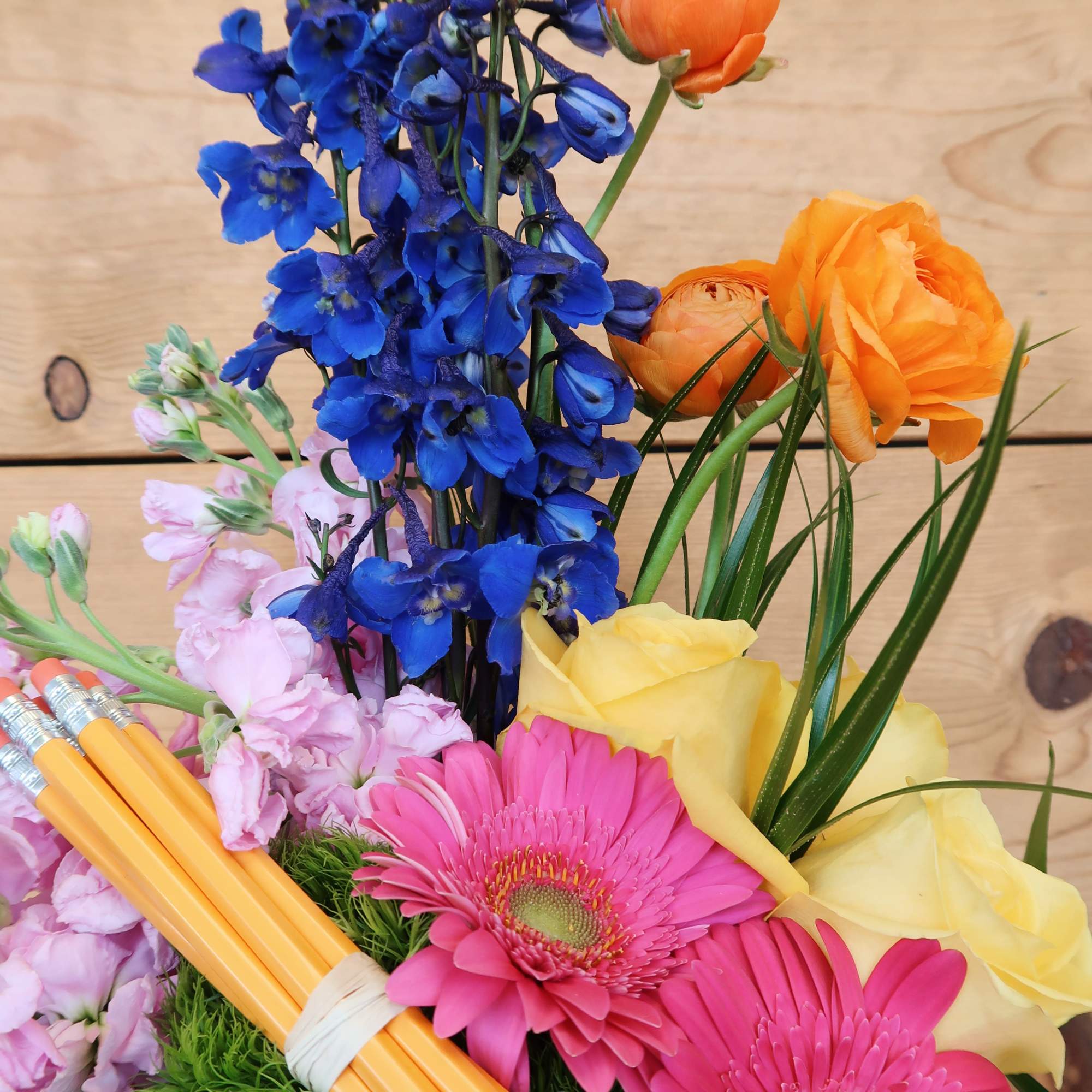 Bouquet of blue delphinium, pink gerbera daisies, and yellow roses with pencils
