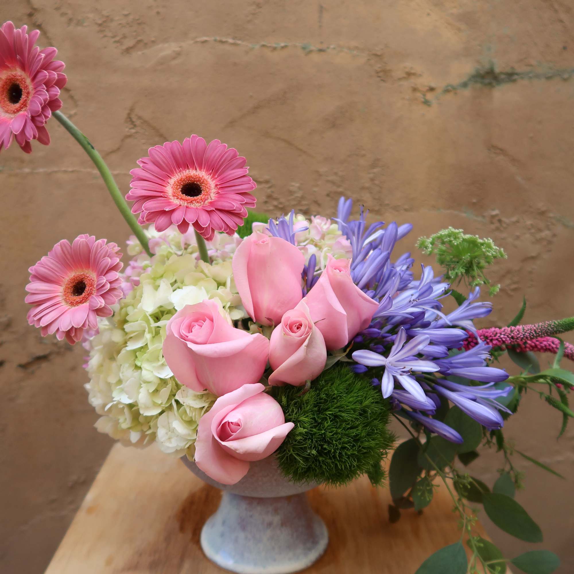 Pink gerbera daisies and roses in a vase with purple flowers