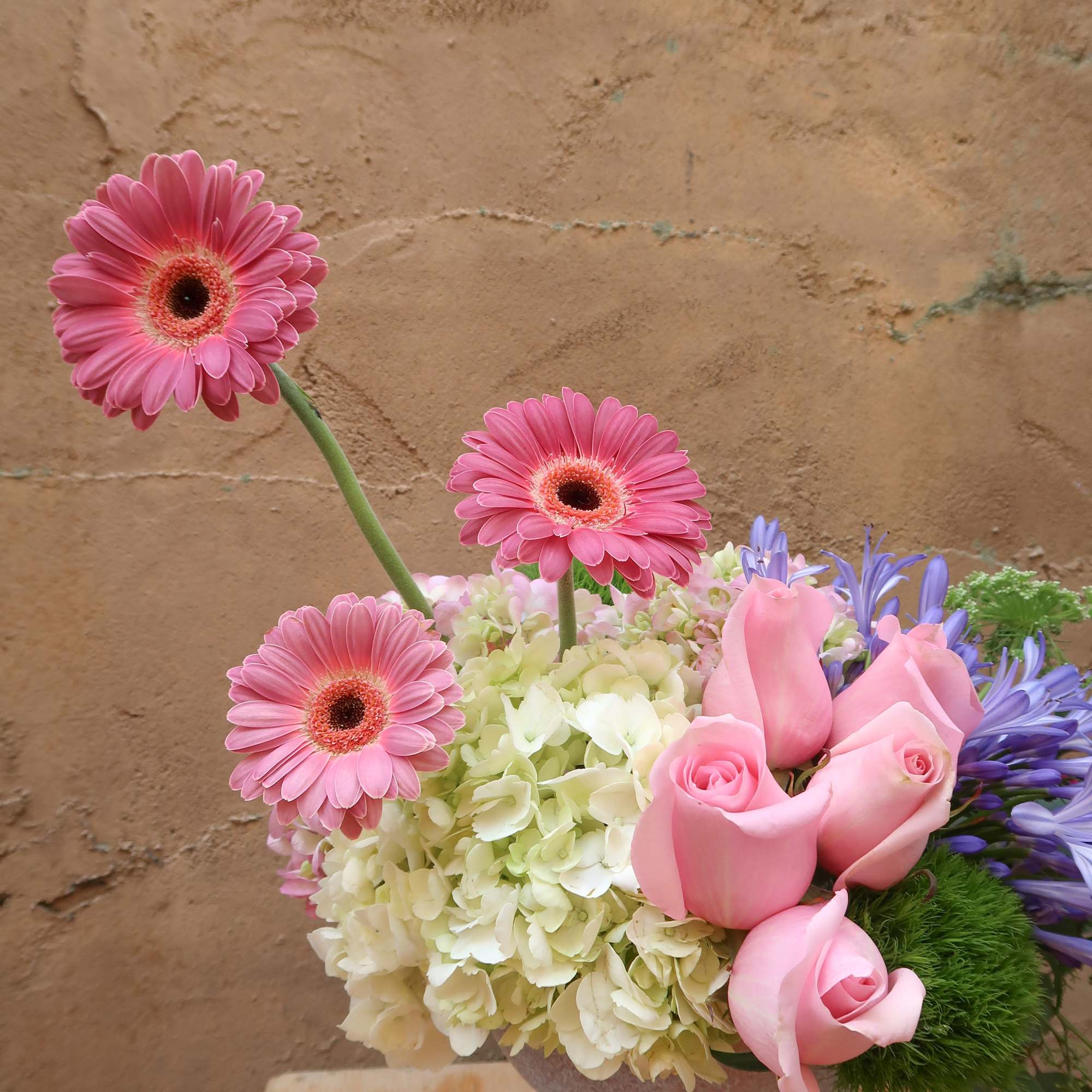 Pink gerbera daisies and roses arranged with hydrangea in a pedestal vase