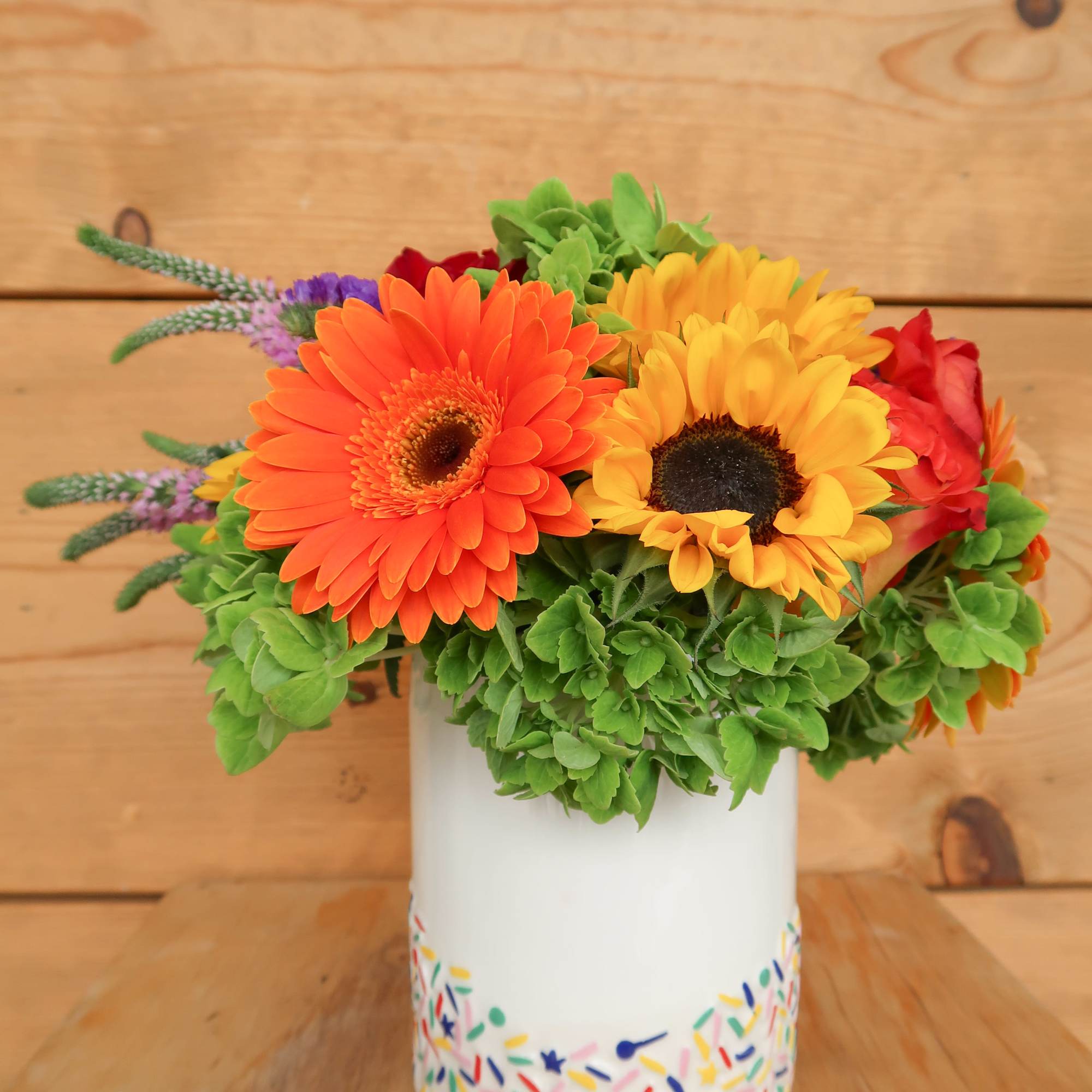 Bright gerbera daisies in a white vase with colorful confetti pattern