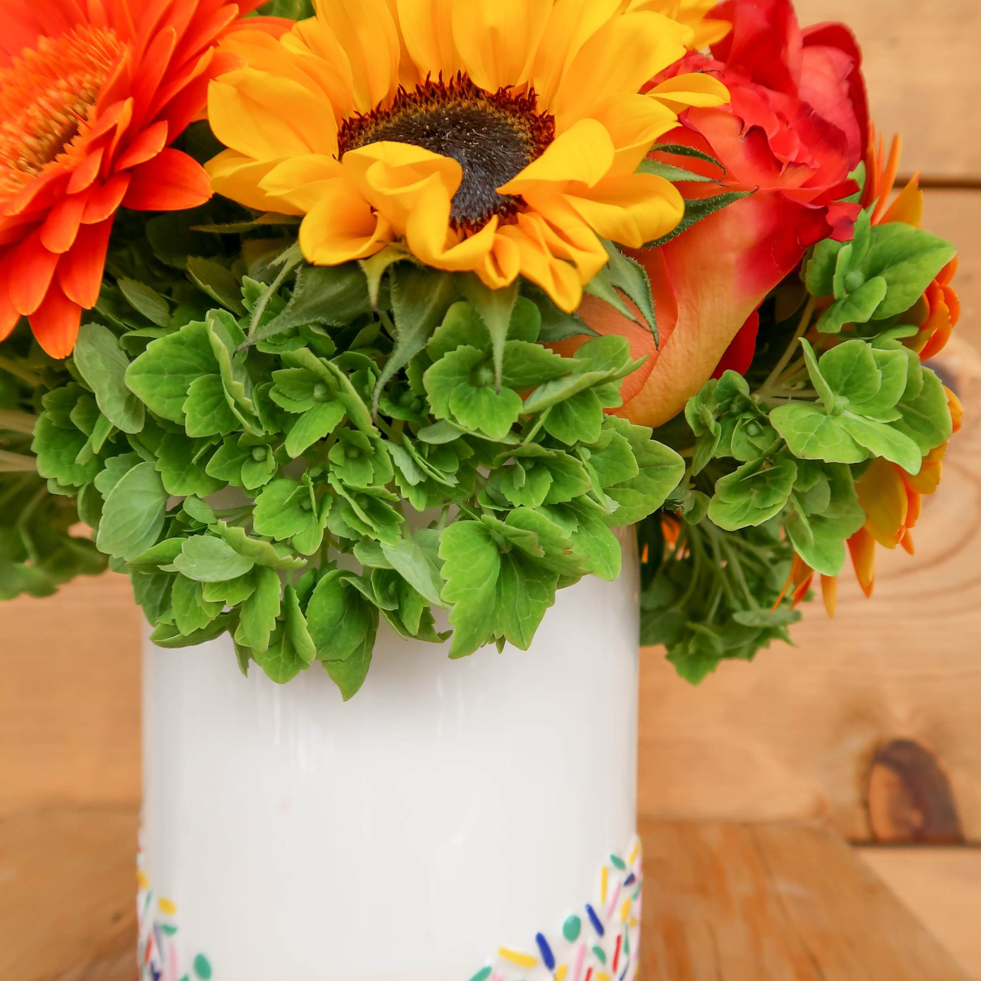 Bright mixed bouquet in a white vase with orange, yellow, and red blooms