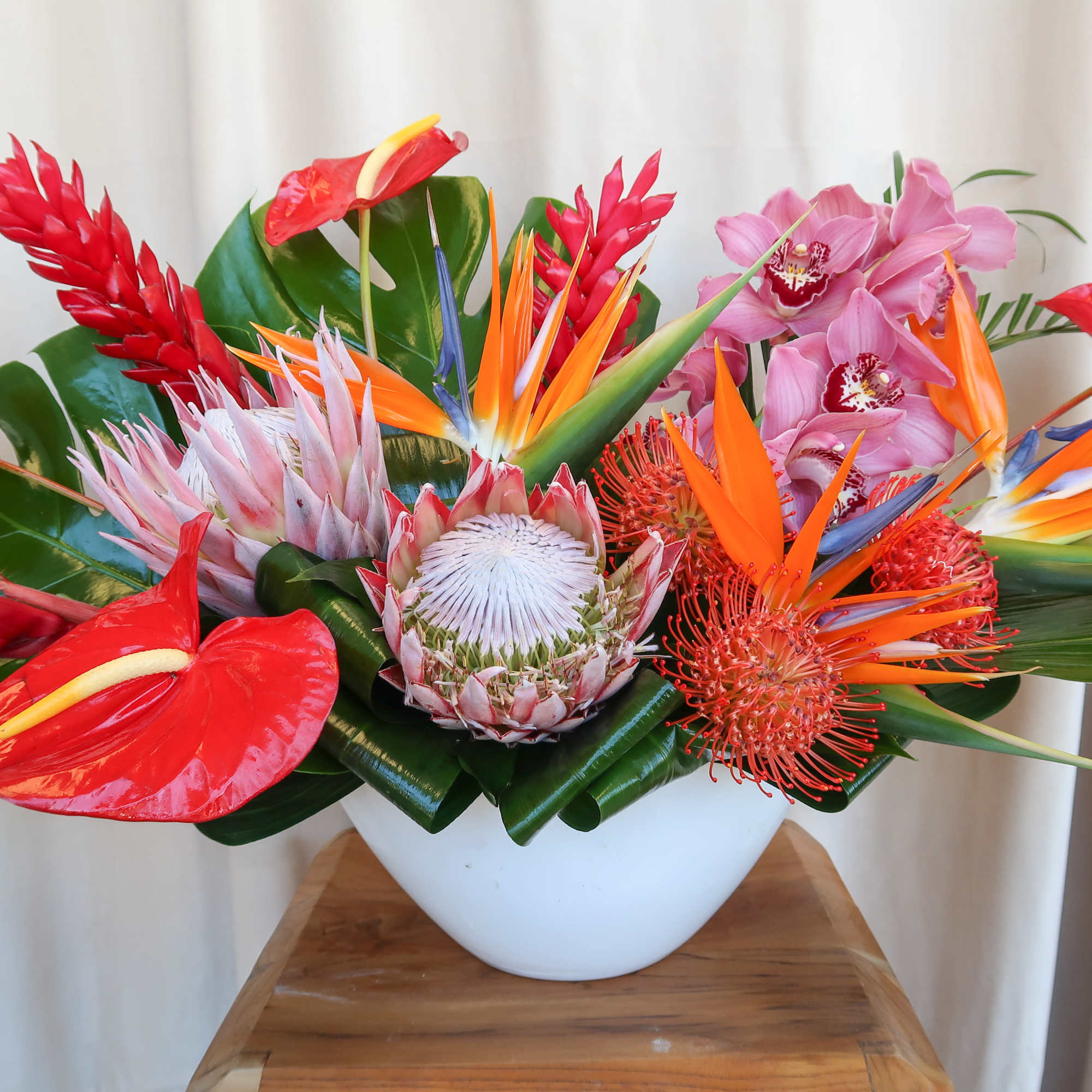 Tropical flower arrangement in a white bowl vase with red, orange, and pink blooms