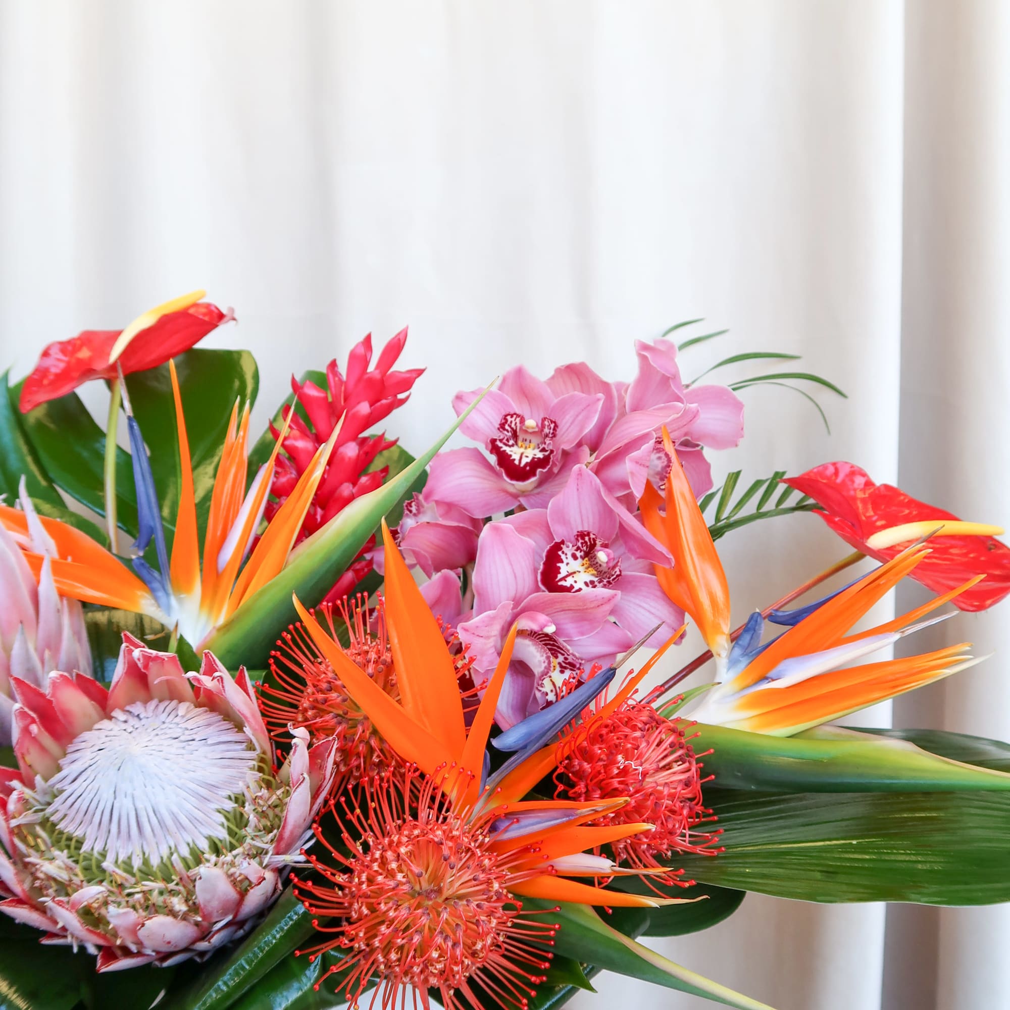 Tropical flower arrangement in a white vase with pink orchids and orange bird-of-paradise