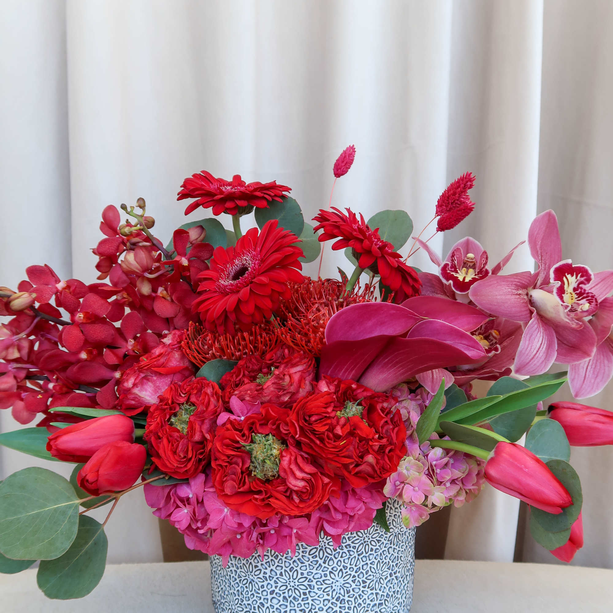 Pink and red mixed flower arrangement in a patterned vase