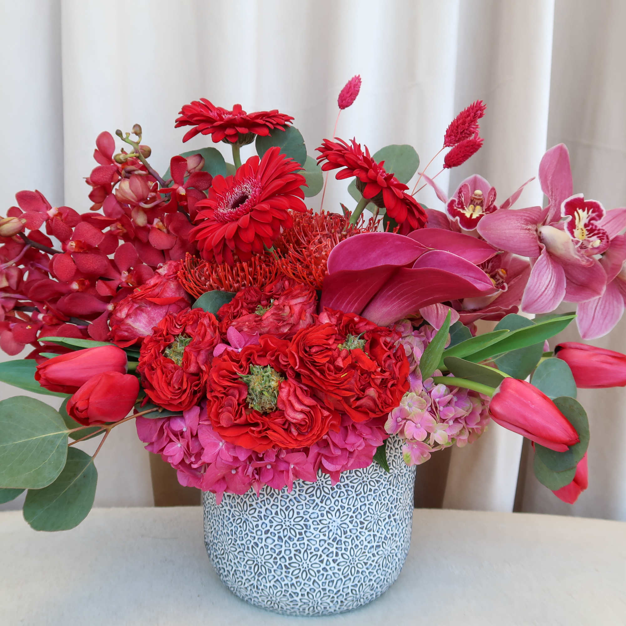 Red and pink floral arrangement in a patterned vase, photo 2 of 6