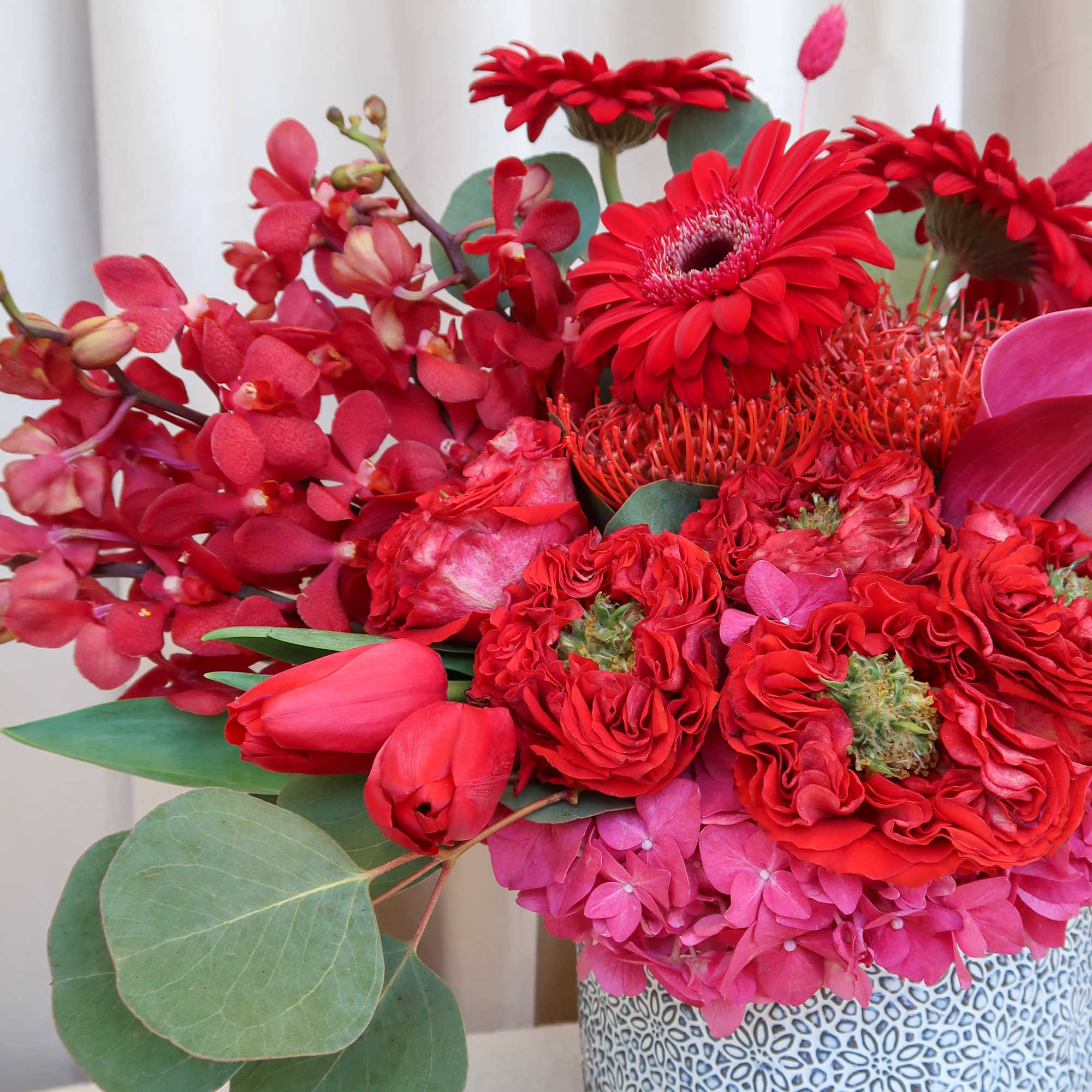 Red floral arrangement in a patterned ceramic pot with pink blooms and eucalyptus