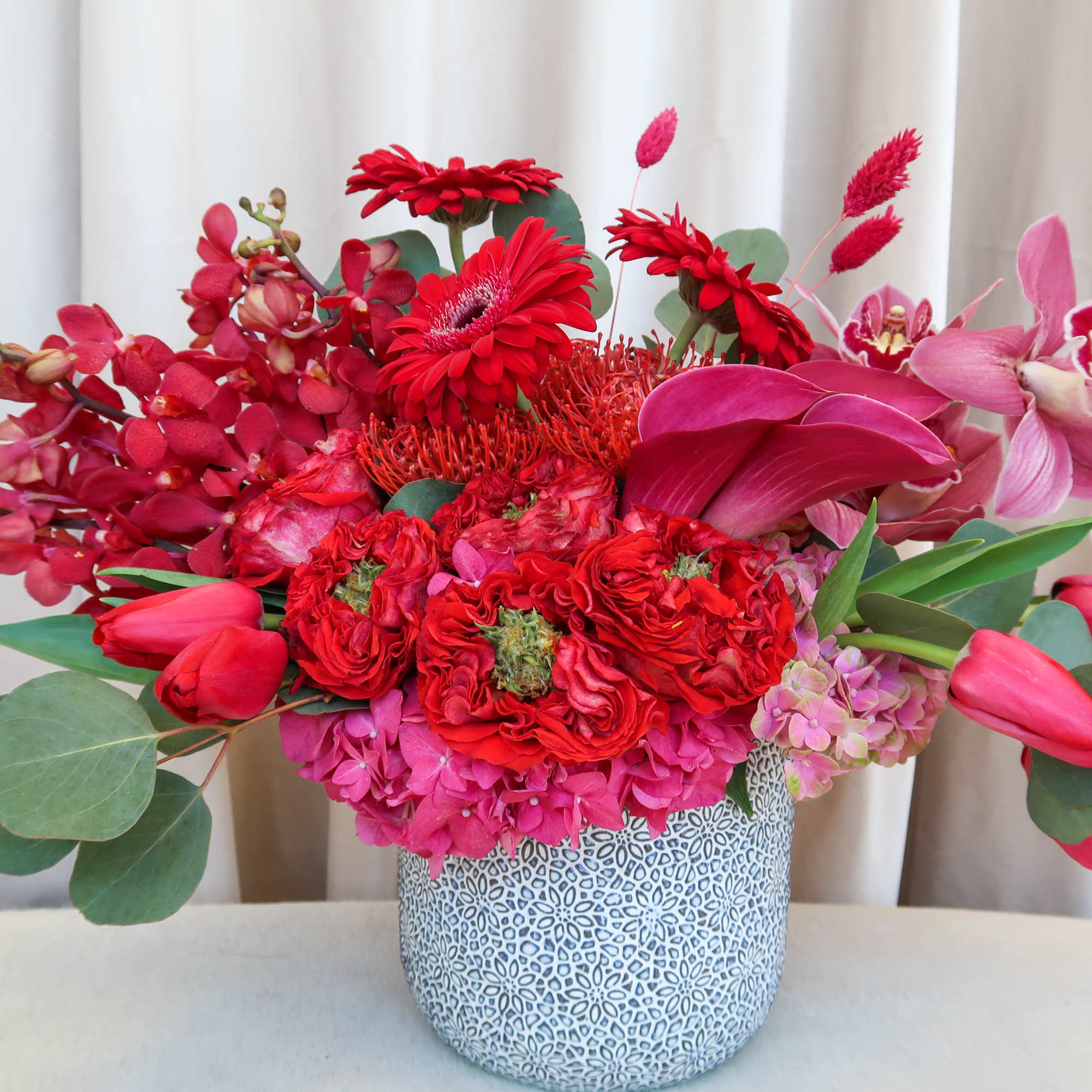 Red and pink floral arrangement in a patterned ceramic vase