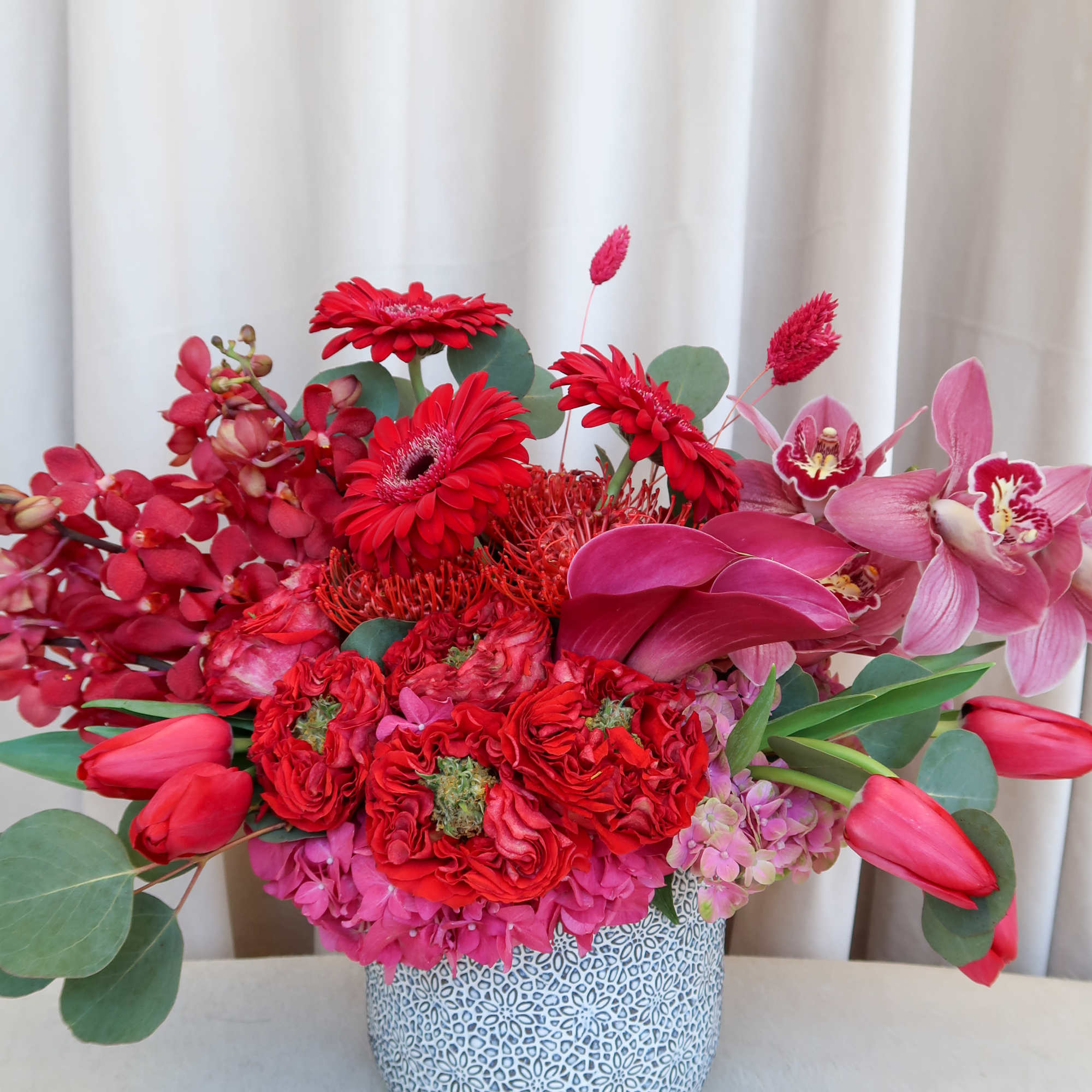 Red and pink floral arrangement in a patterned vase, photo 5 of 6