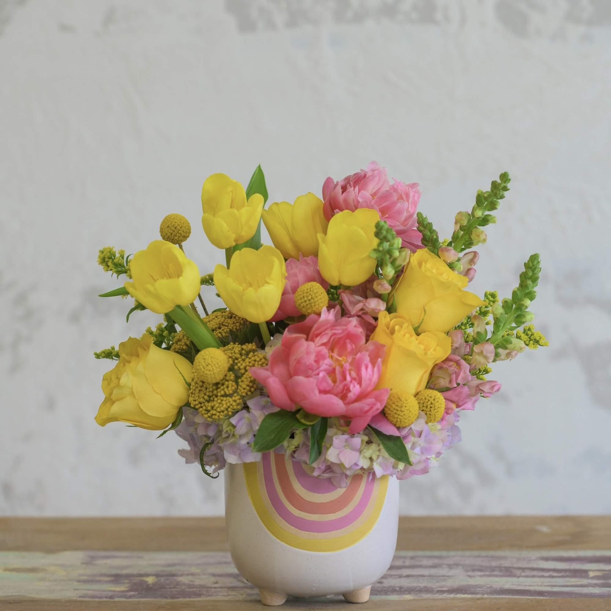 Yellow tulips and pink flowers in a white ceramic vase