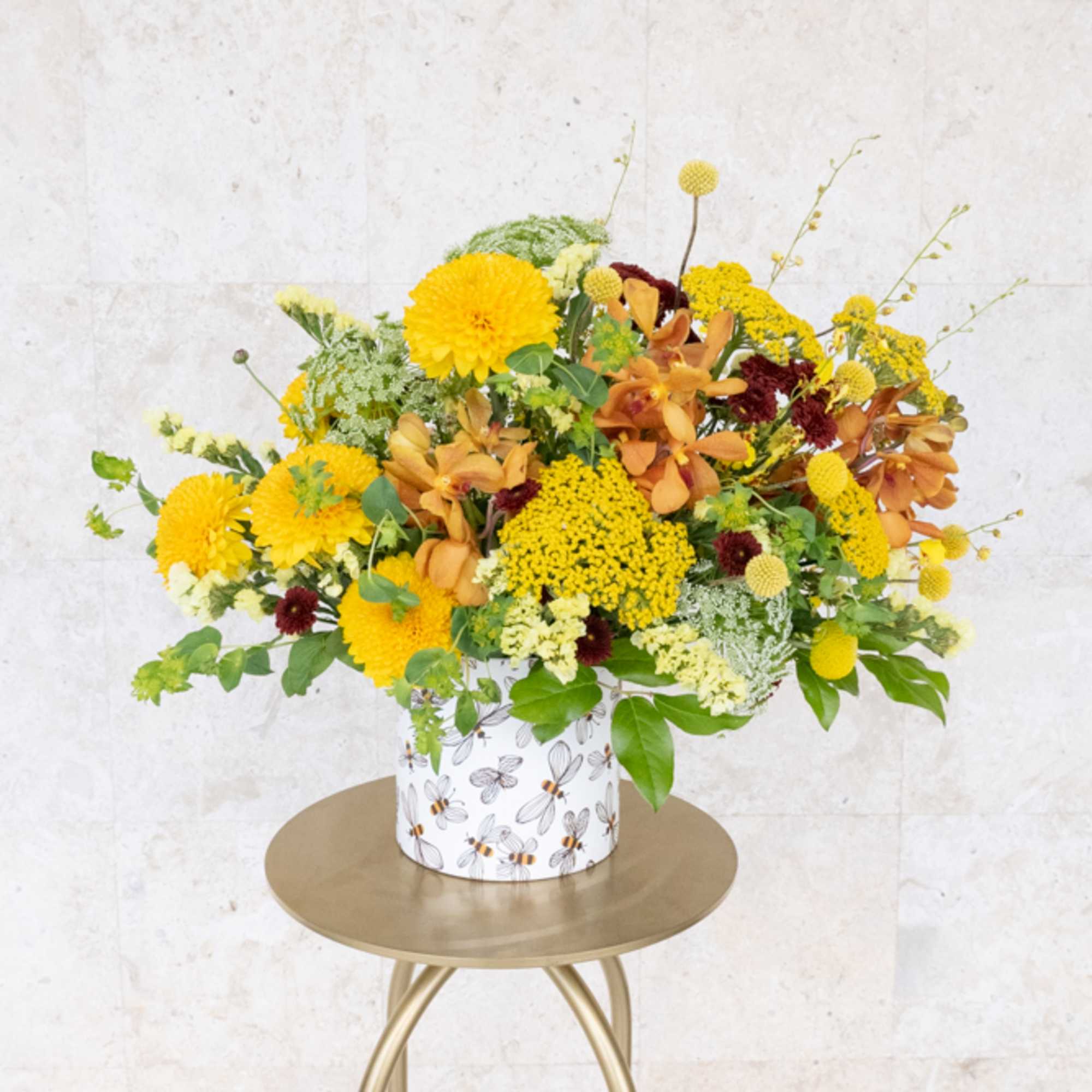 Yellow and orange mixed flower arrangement in a patterned container on a small table